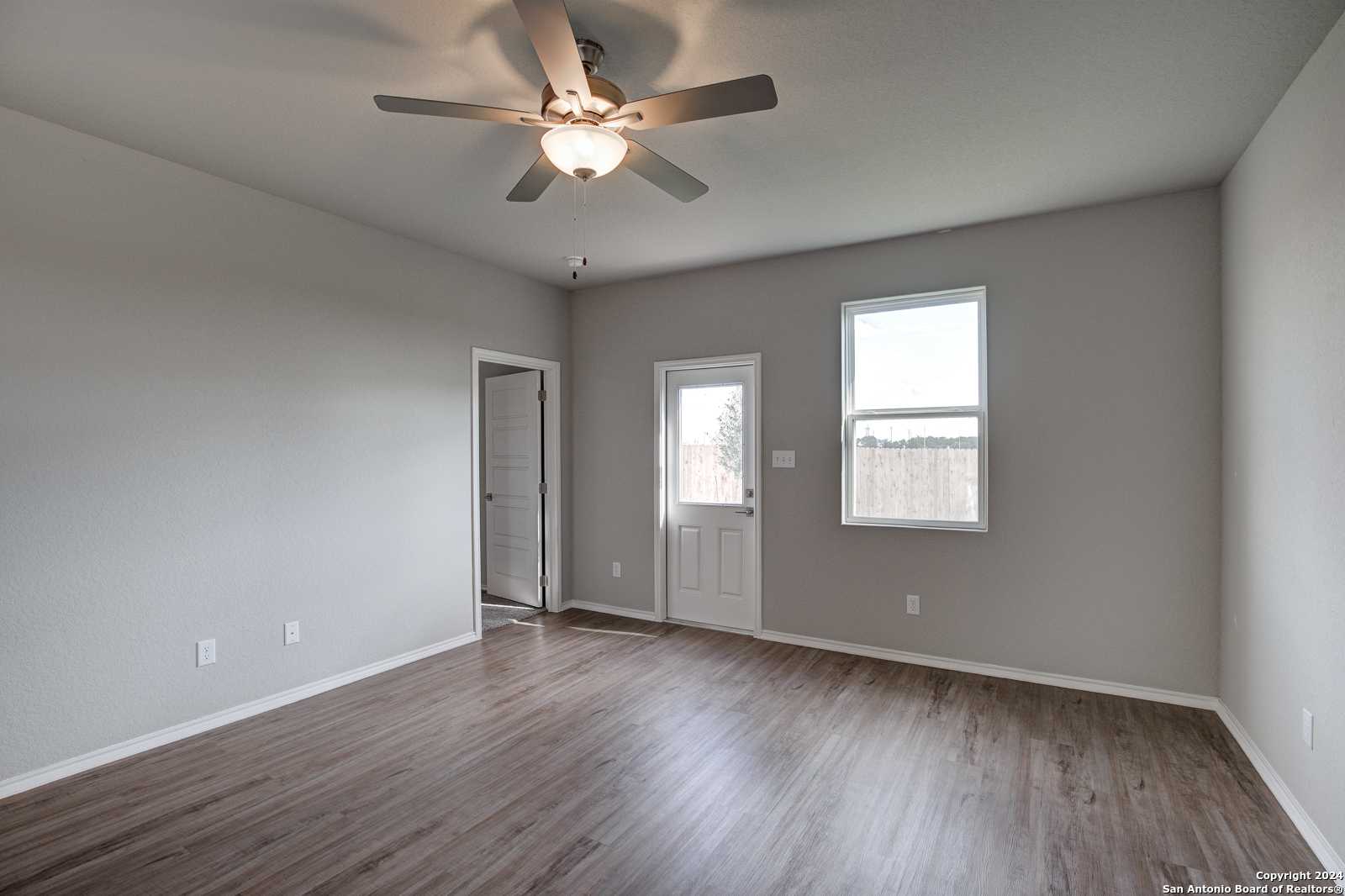 Bright master bedroom with gray walls, hardwood floors, ceiling fan, and patio access in Davidson Homes The Frio B, San Antonio