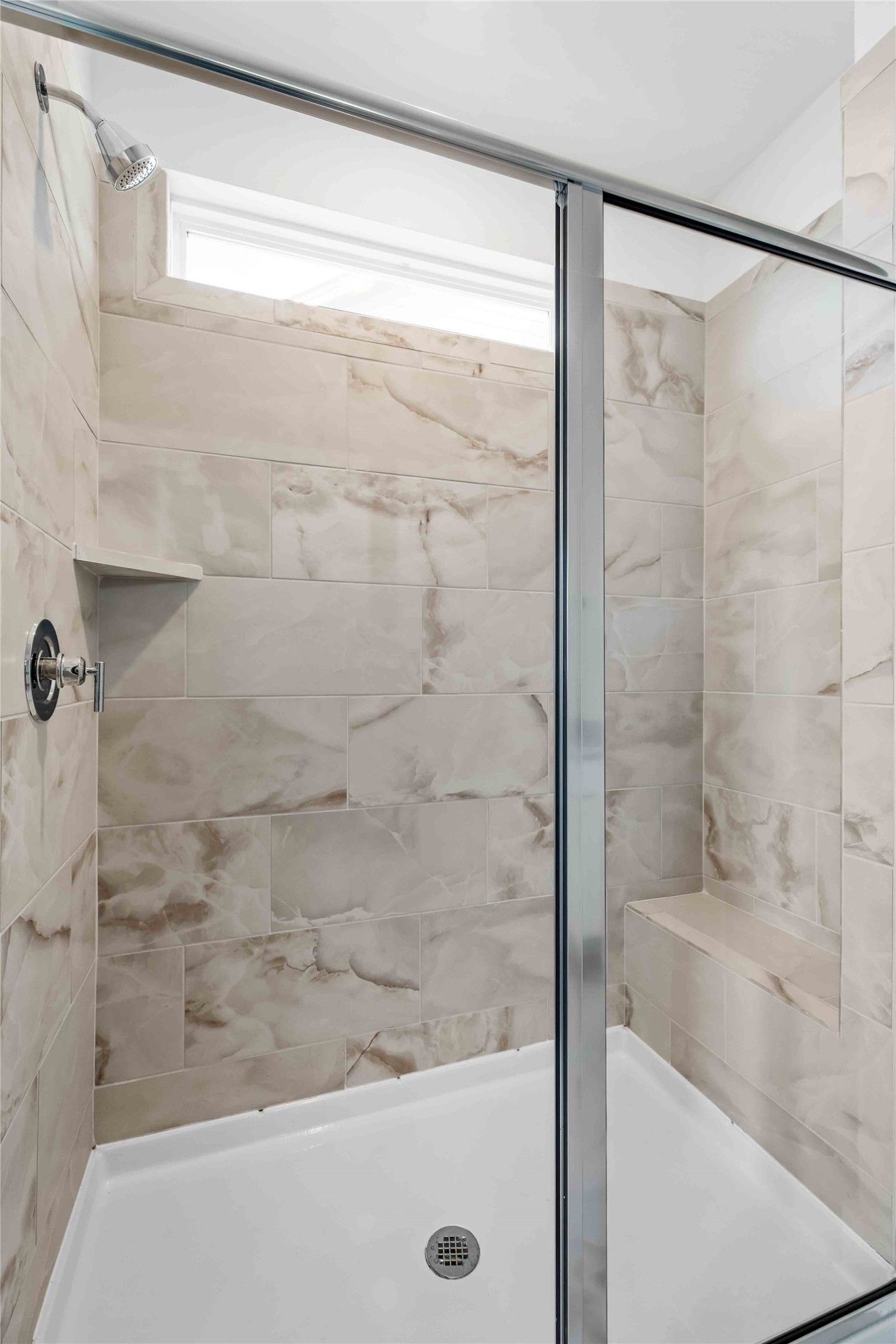 Modern walk-in shower with marble-look tile and built-in bench in The Ash O floor plan by Davidson Homes in Heartland, TX.