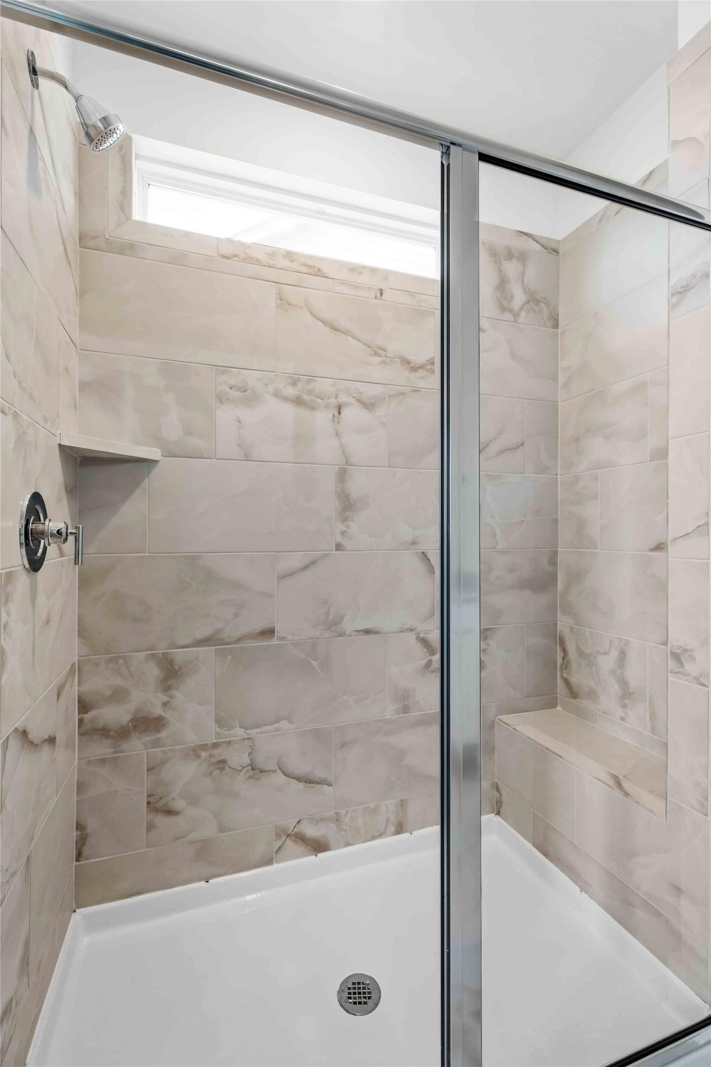 Modern walk-in shower with marble-look tile and built-in bench in The Ash O floor plan by Davidson Homes in Heartland, TX.