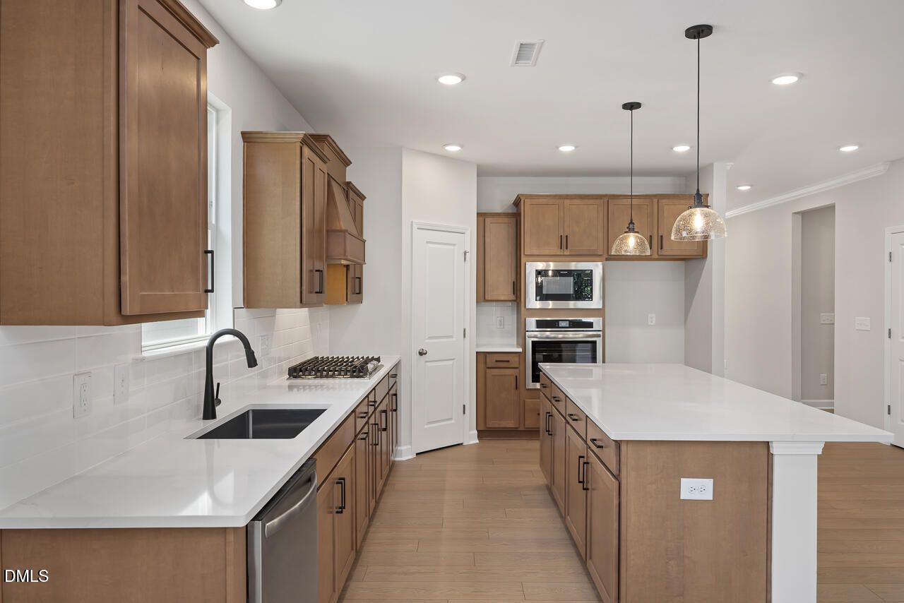 Modern kitchen with wood cabinets, quartz countertops, and large island in The Ashport L at Sage on North Main, Wake Forest.