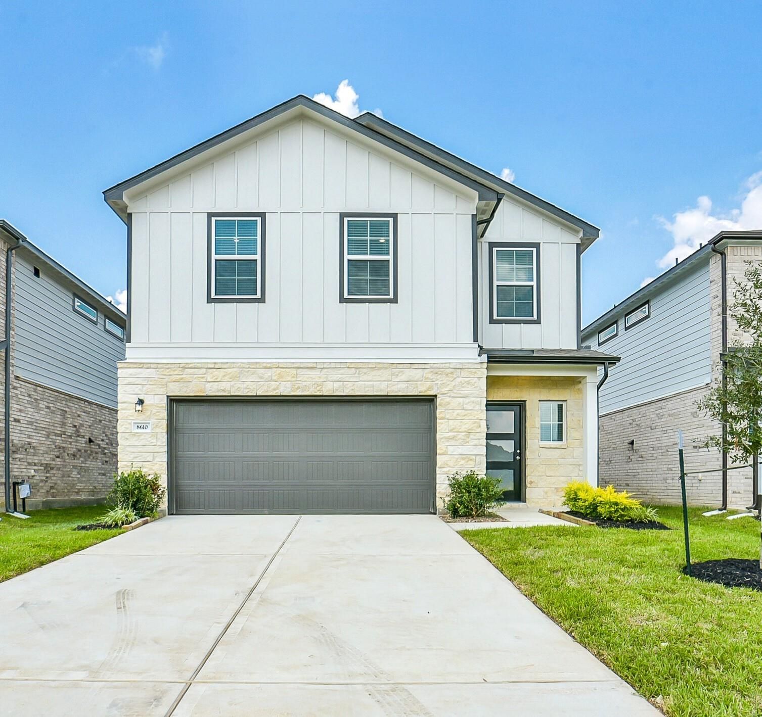 Modern two-story Davidson Homes Blanco E with white shiplap, stone accents, 2-car garage, driveway, and lush landscaping in Lakes at Black Oak, Magnolia, Texas