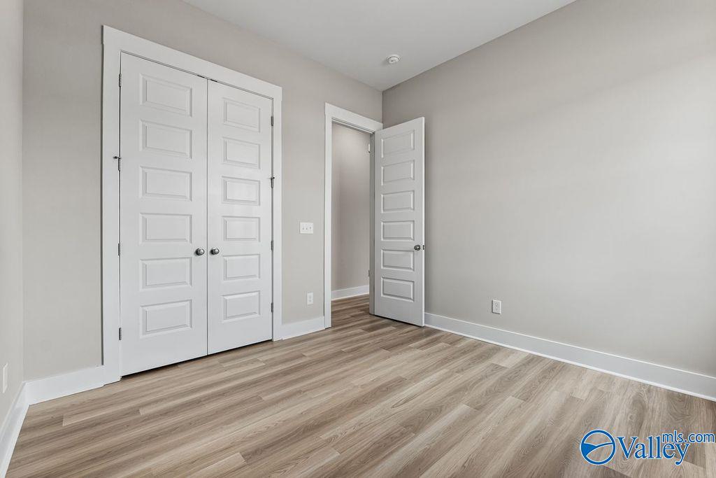 Spacious secondary bedroom featuring double closet doors, open bathroom access, and light wood flooring in Evermore Homes The Oxford, Owens Cross Roads, Alabama