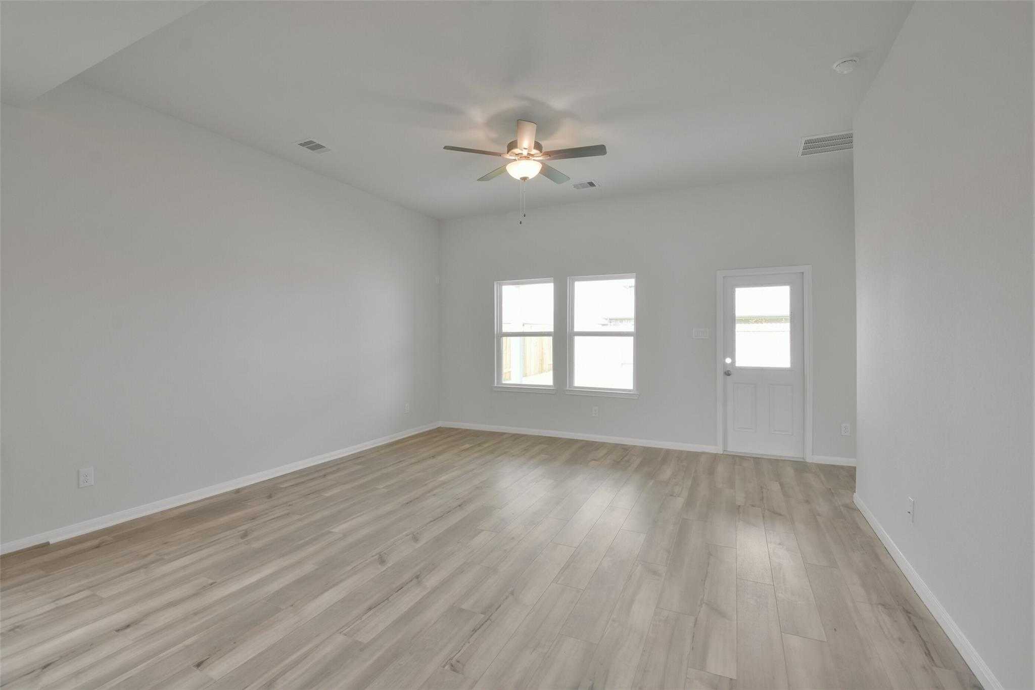 Bright bedroom with ceiling fan, double windows, white walls, and light wood floors in Davidson Homes The Tierra A, Dayton, Texas