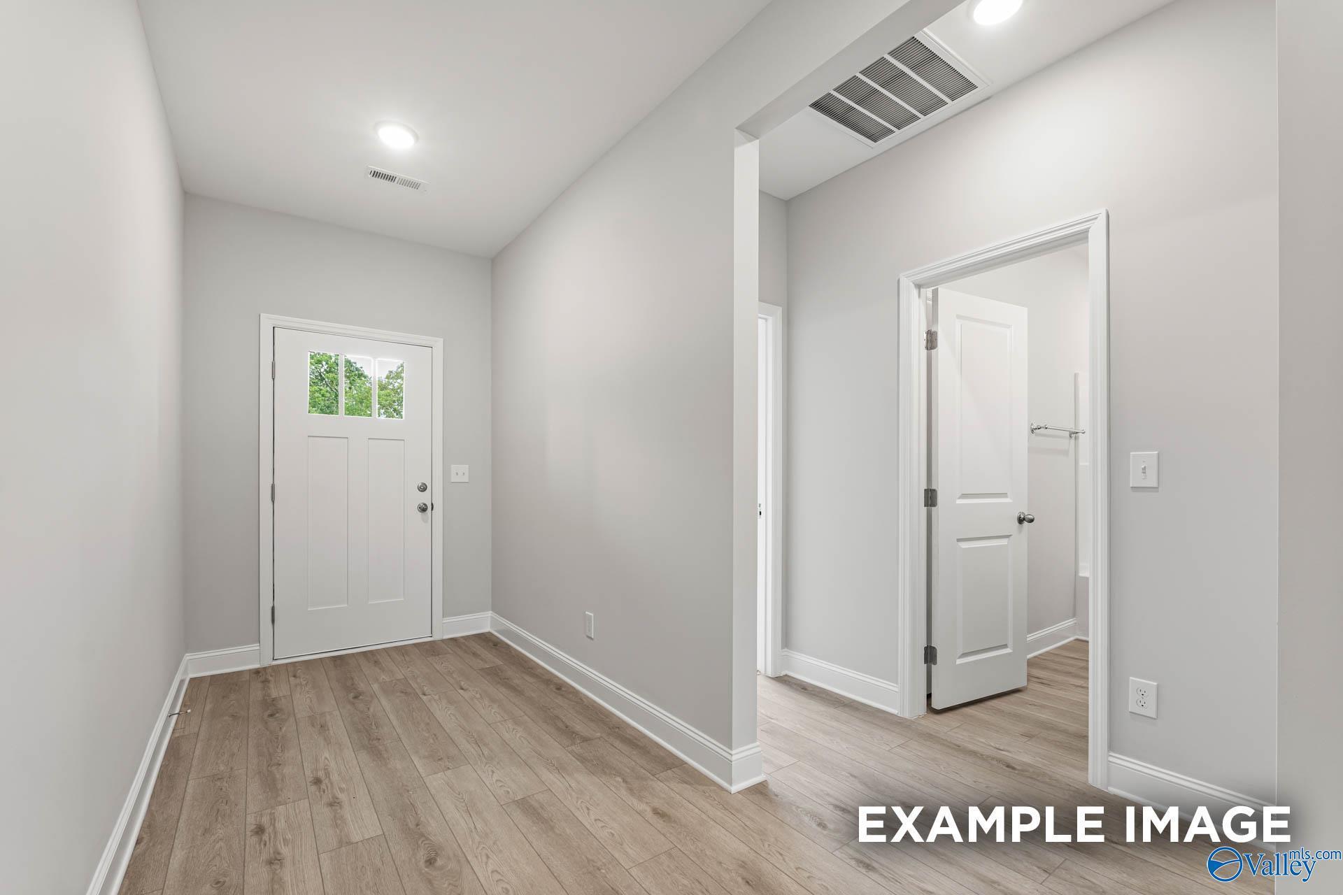 Bright entryway hallway with light wood floors, white doors, and front entrance in Davidson Homes The Daphne, Hazel Green AL