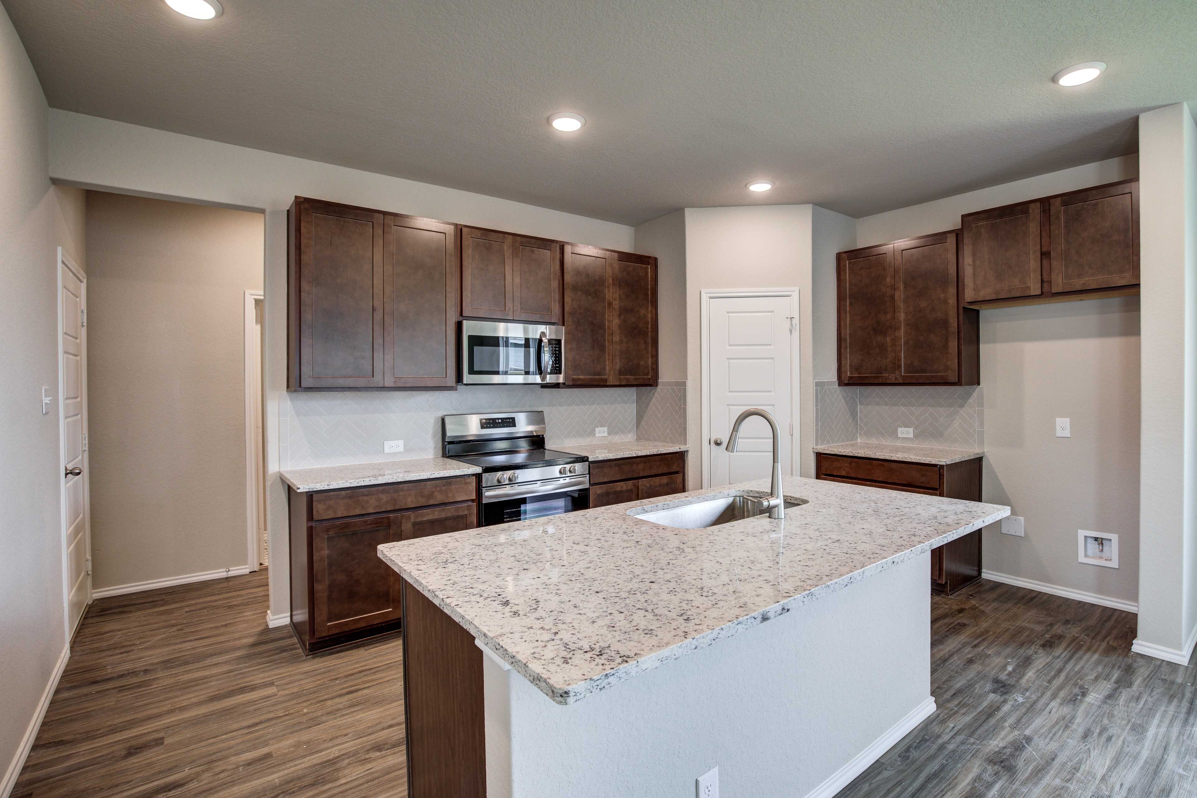 Gourmet kitchen in The Murray home featuring quartz island sink, dark shaker cabinets, stainless steel appliances, wood floors