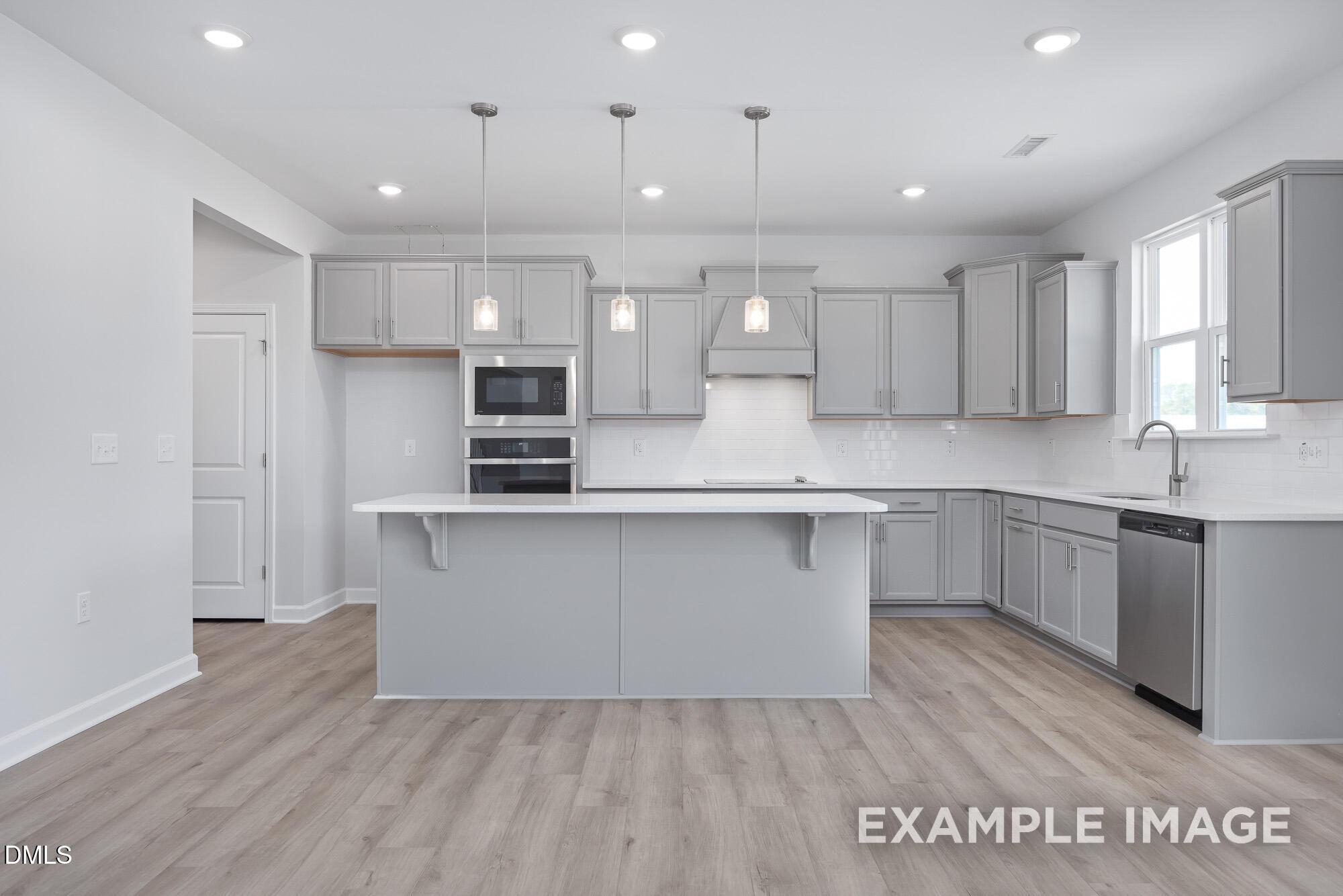 Modern open-concept kitchen featuring gray shaker cabinets, oversized island, stainless steel appliances in Davidson Homes Hickory II B, Lillington NC
