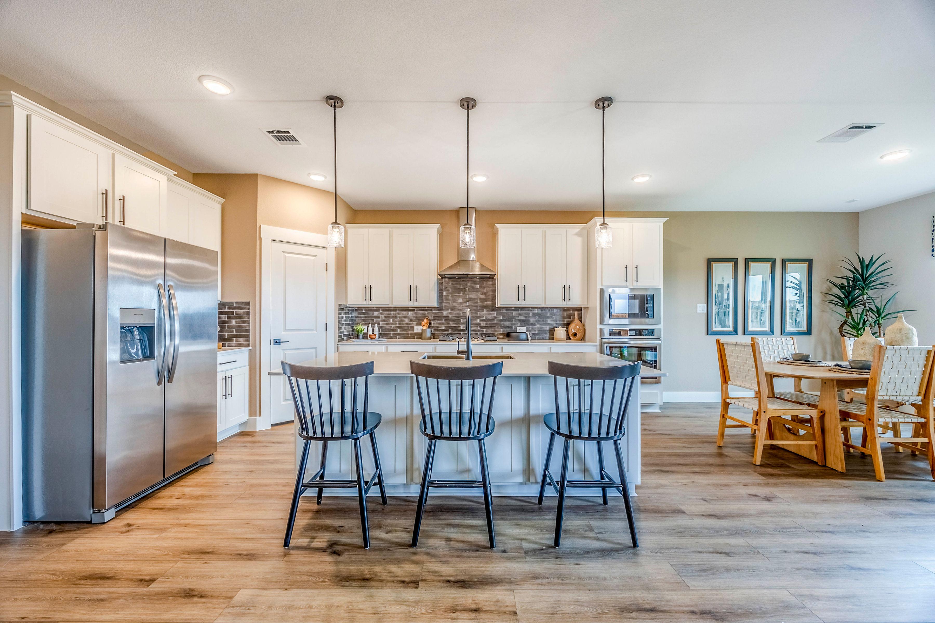 Spacious open-concept kitchen at Waverly Estates in Josephine TX with white cabinets, stainless appliances, island bar, and hardwood floors