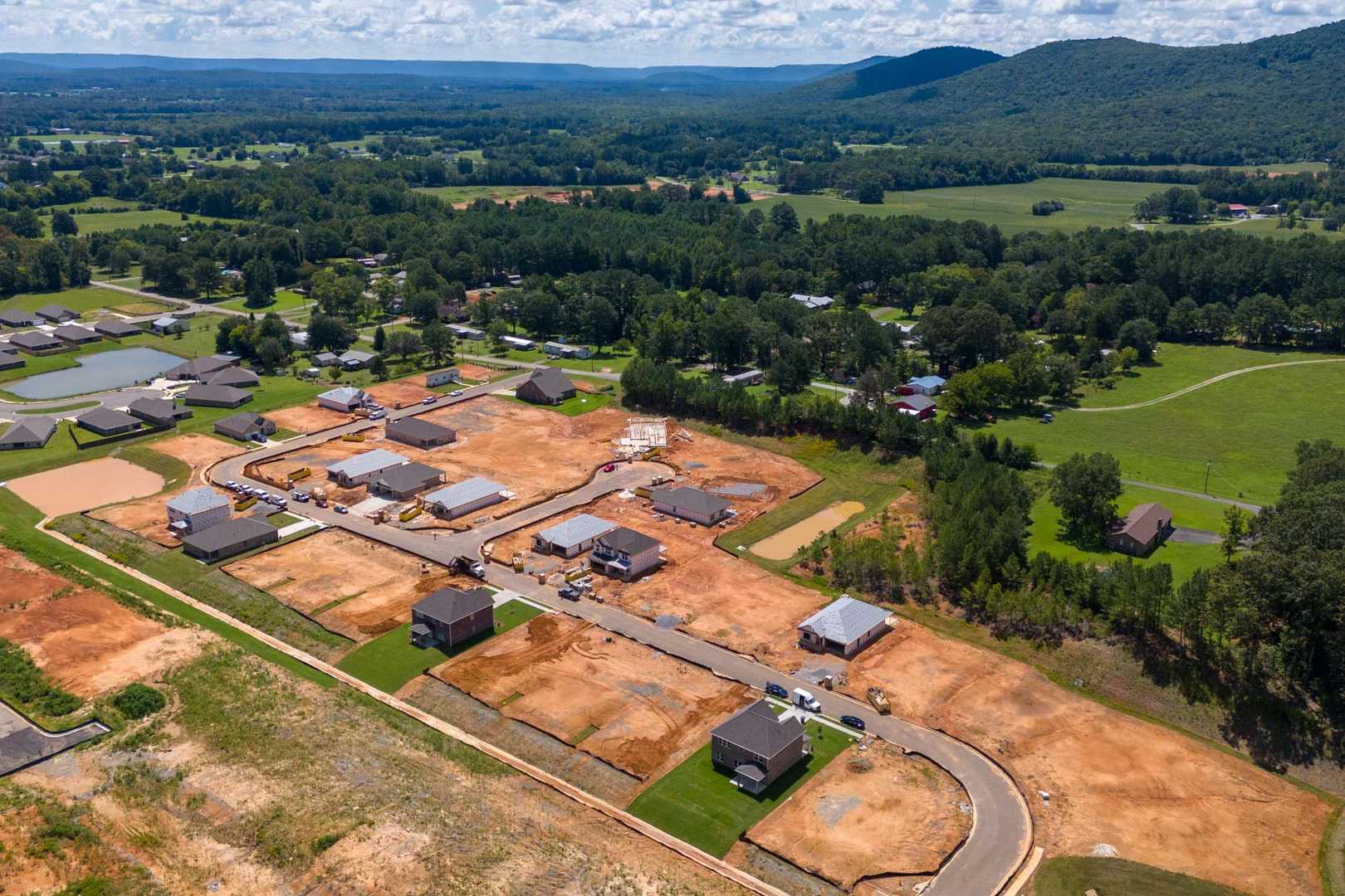 Aerial view of new homes under construction at Watts Glen in Owens Cross Roads, Alabama with wooded fields and mountains