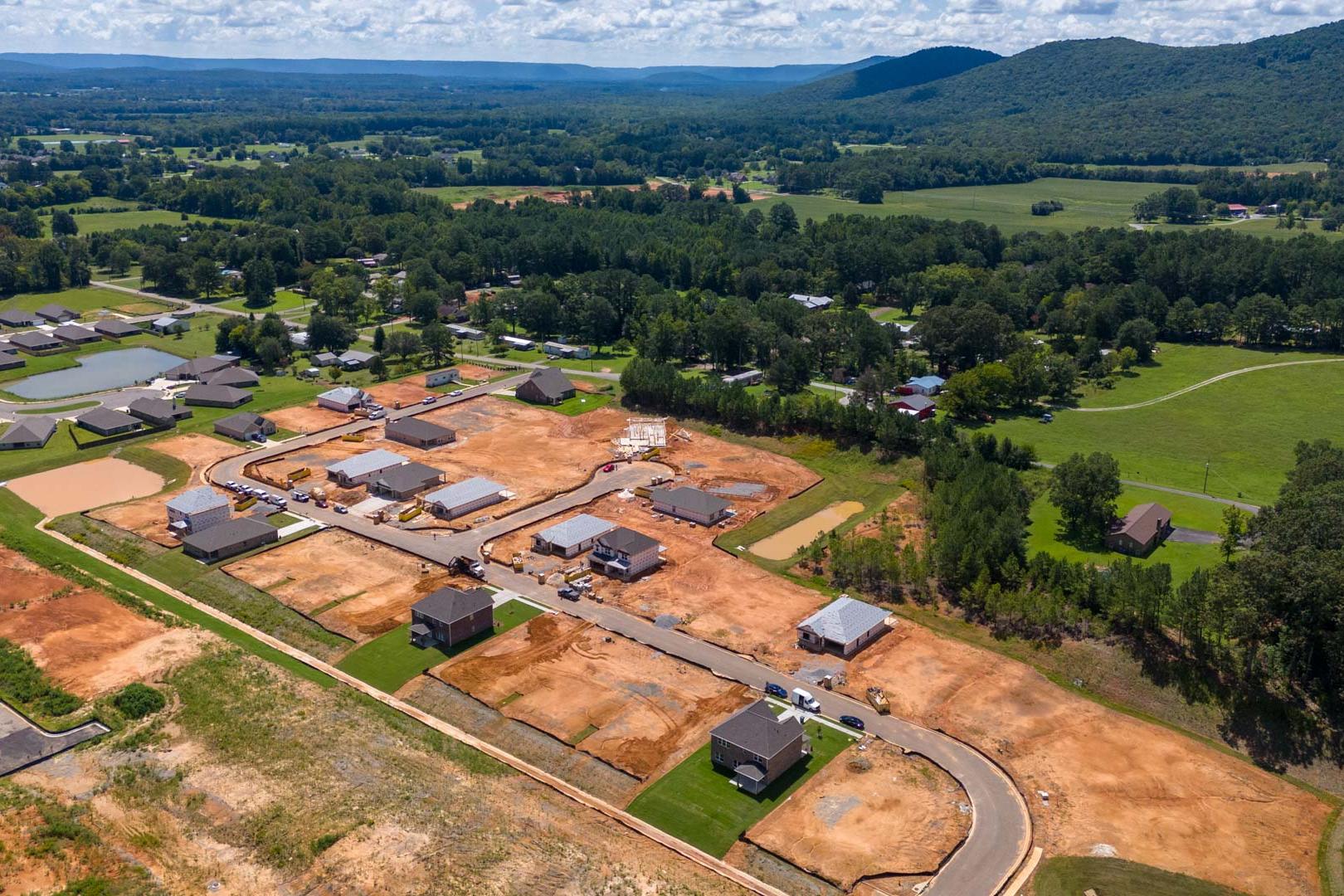 Aerial view of new homes under construction at Watts Glen in Owens Cross Roads, Alabama with wooded fields and mountains