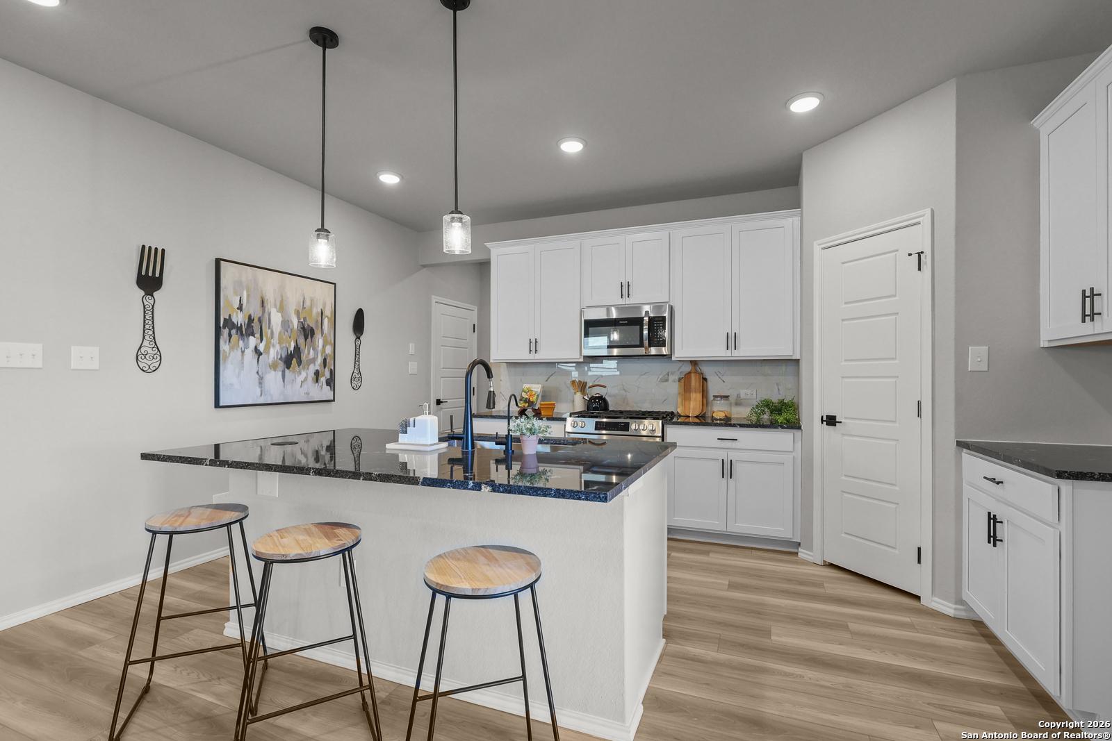 Modern kitchen with white shaker cabinets, black granite island, stainless appliances, and pendant lights in Davidson Homes The Murray K, San Antonio