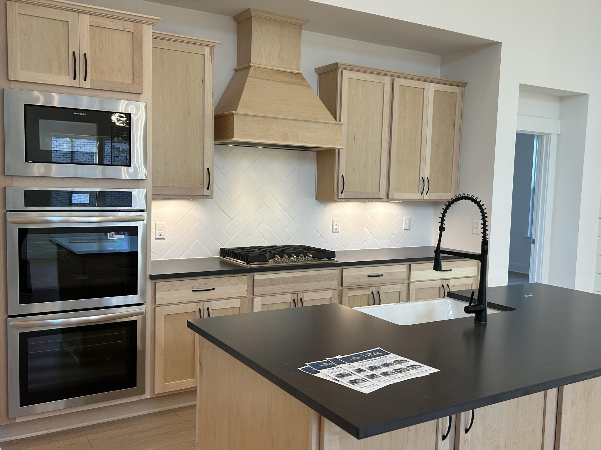 Elegant kitchen with light oak cabinets, black quartz counters, stainless double ovens, gas cooktop in Davidson Homes The Ridgeport E, Mt. Juliet, TN