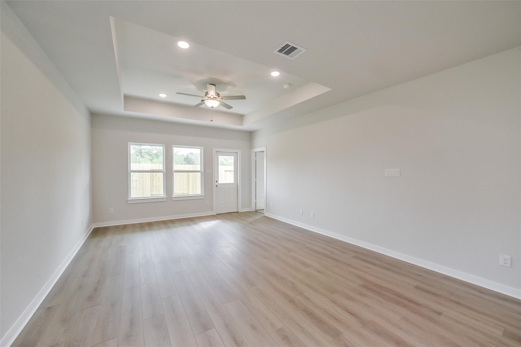 Spacious living room with tray ceiling, ceiling fan, large windows, French doors and laminate floors in Davidson Homes The Frio F, Conroe, Texas
