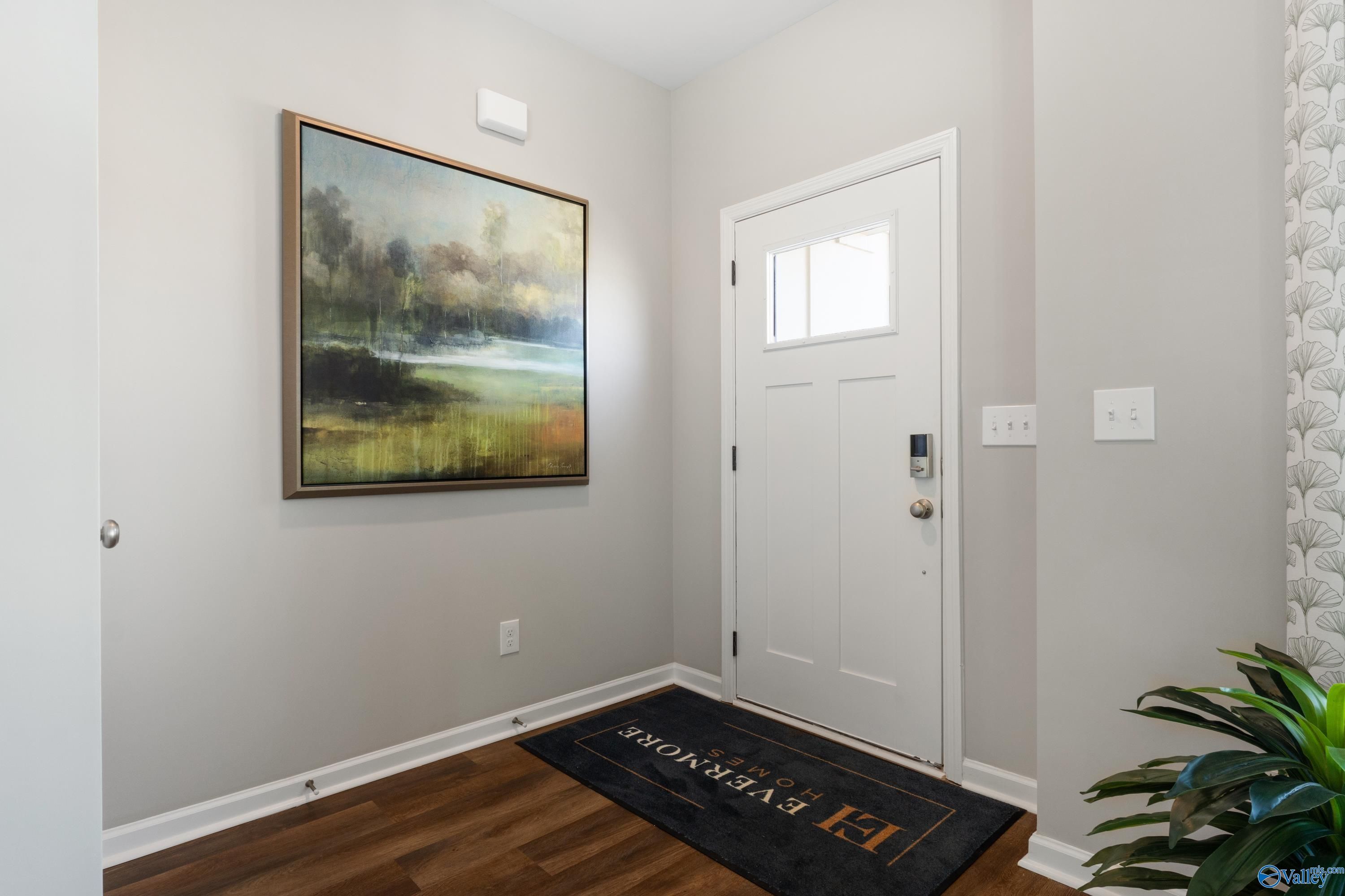 Welcoming entry foyer with white paneled door, framed landscape artwork, hardwood floors, and Davidson Homes doormat in The Stella, Evergreen Mill, Madison, Alabama