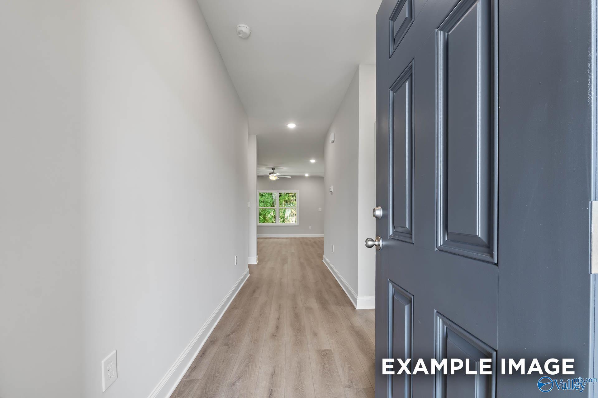 Bright entry hallway with light wood floors, white walls, and dark front door in Davidson Homes The Asheville, Toney, AL
