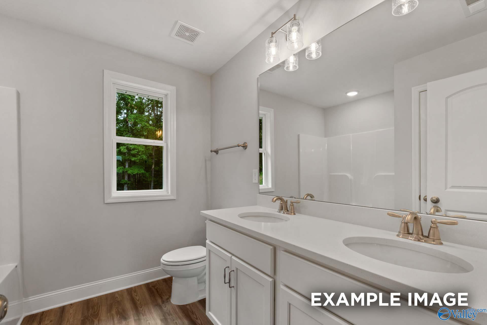 Modern bathroom with double white quartz vanity, gold faucets, large mirror, and window view in Davidson Homes The Shelby C, Arab, Alabama