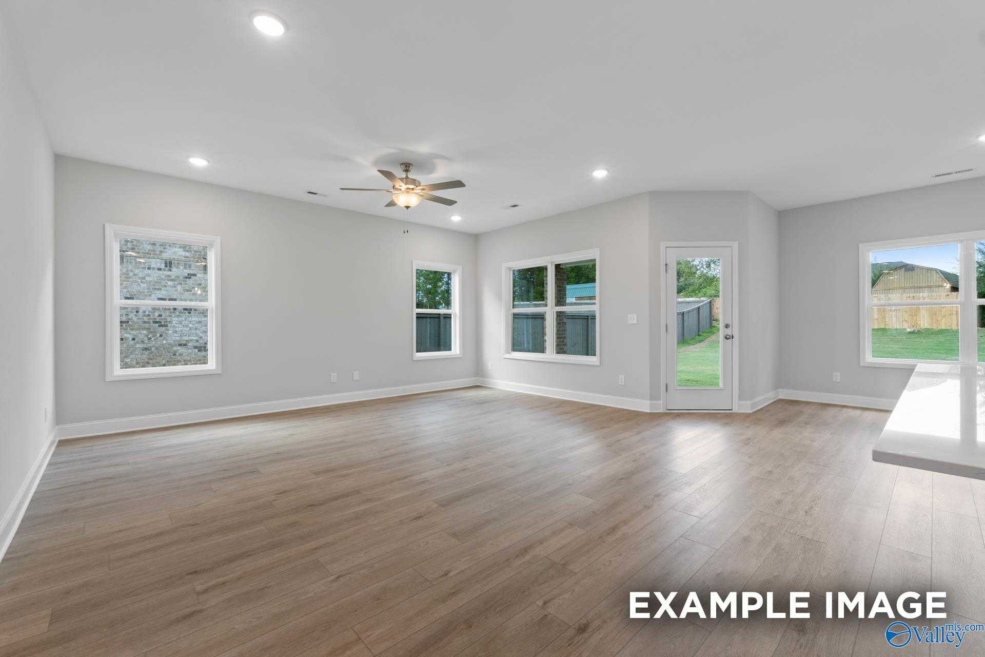 Bright open living room with hardwood floors, ceiling fan, large windows, and sliding doors to backyard in Davidson Homes The Franklin V, Athens, Alabama