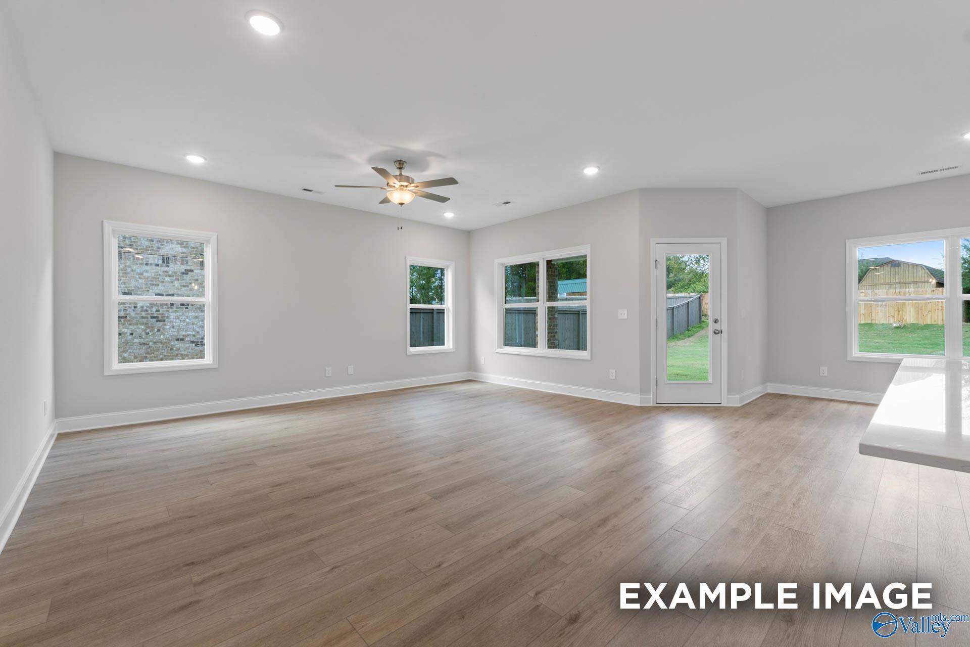 Bright open living room with hardwood floors, ceiling fan, large windows, and sliding doors to backyard in Davidson Homes The Franklin V, Athens, Alabama