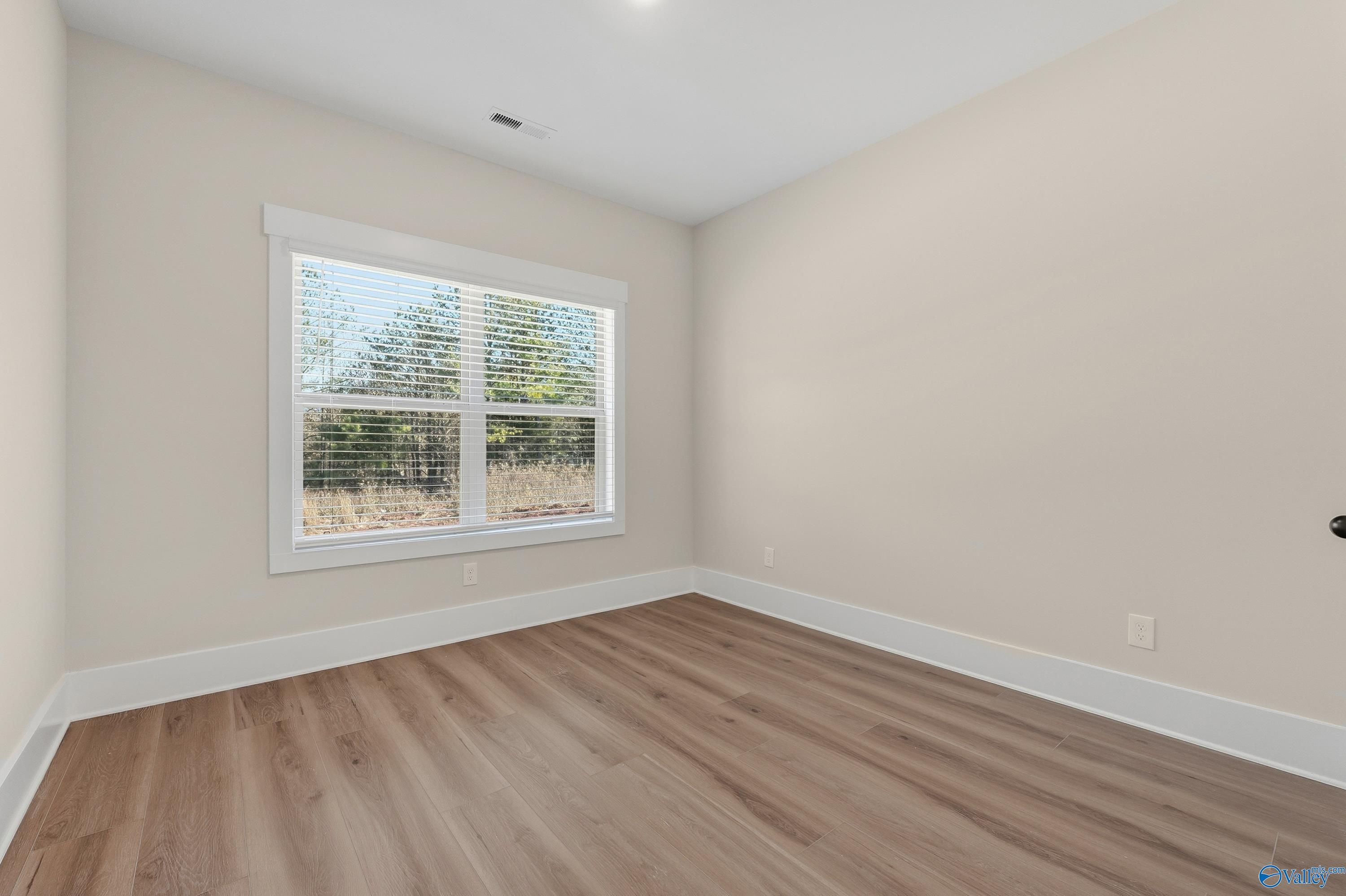 Bright secondary bedroom featuring light hardwood floors, neutral walls, and large window with wooded view in The Shelby A, Athens AL