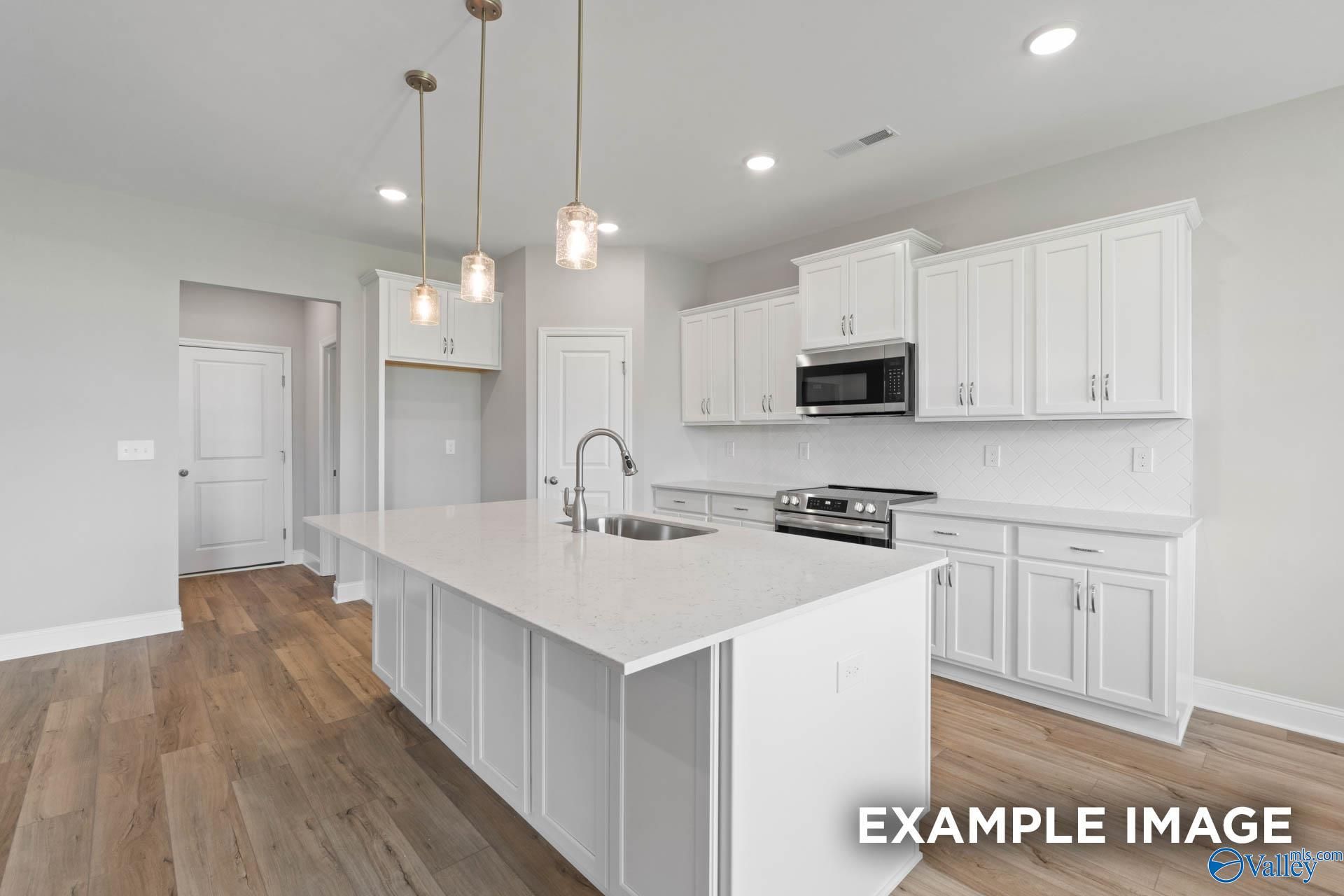 Modern white kitchen island with farmhouse sink, stainless appliances, and pendant lights in The Montgomery B, Hartselle, AL