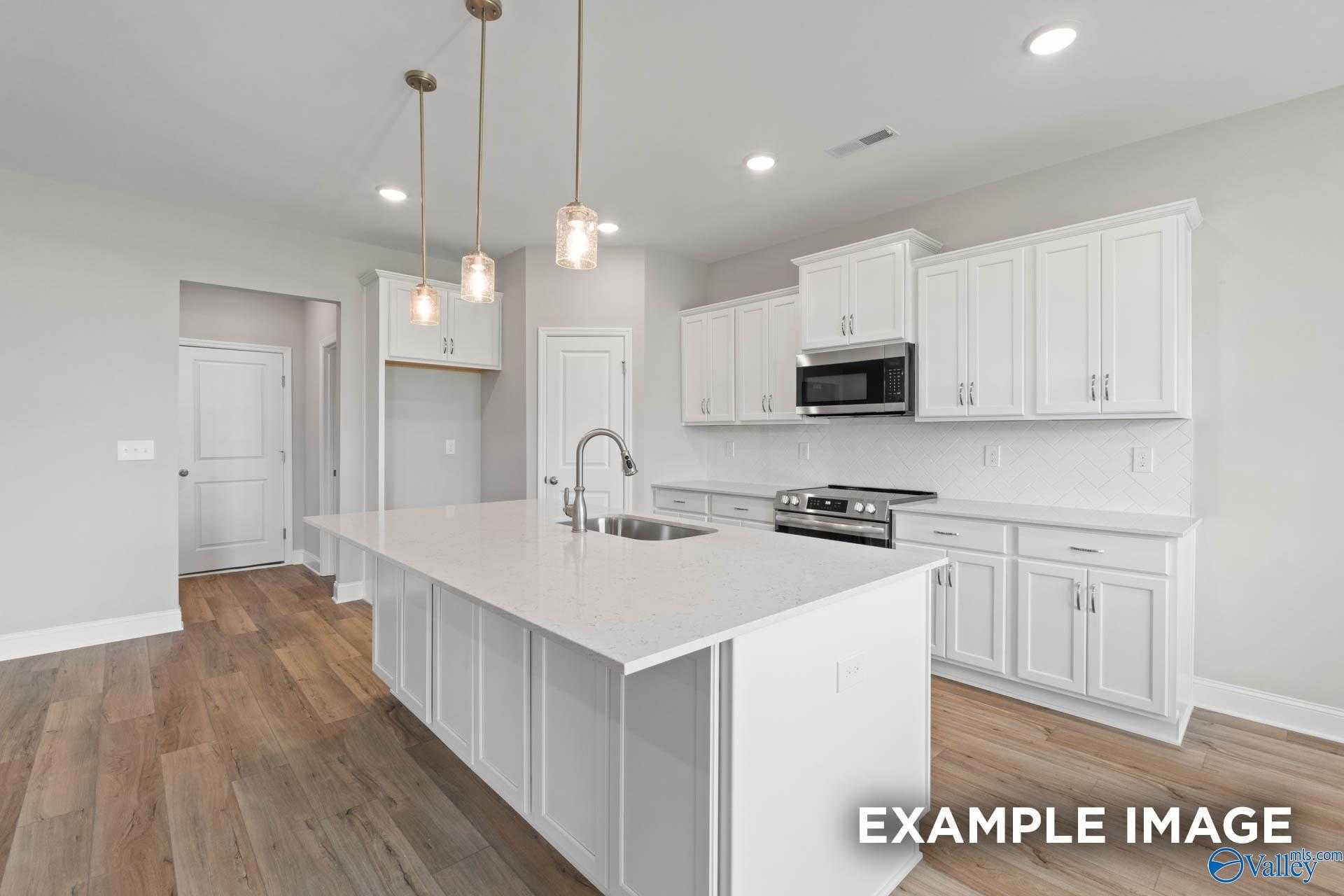 Modern white kitchen island with farmhouse sink, stainless appliances, and pendant lights in The Montgomery B, Hartselle, AL