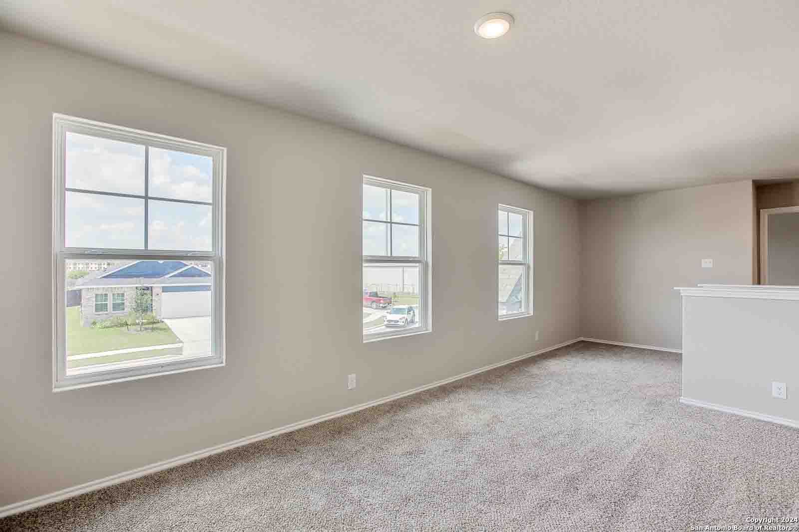 Bright living room with large windows overlooking neighborhood, beige walls and carpet in 4-bedroom Davidson Homes The Murray H, Seguin, Texas