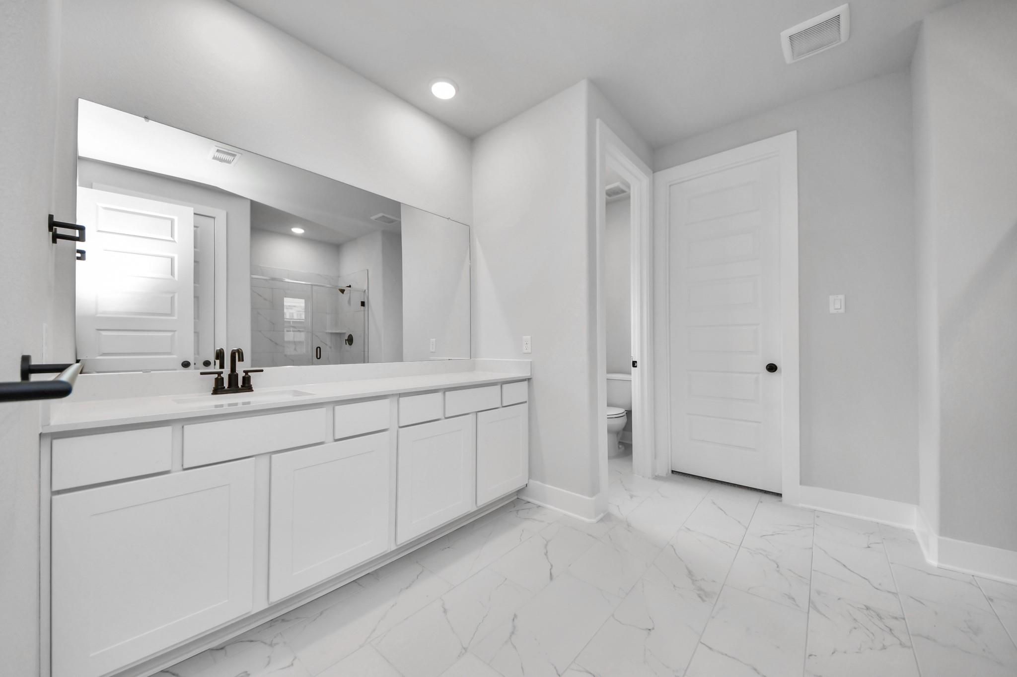 Modern bathroom with white dual vanity, marble-style tile floors, and dark fixtures in The Laguna C home, Sunterra, Katy.