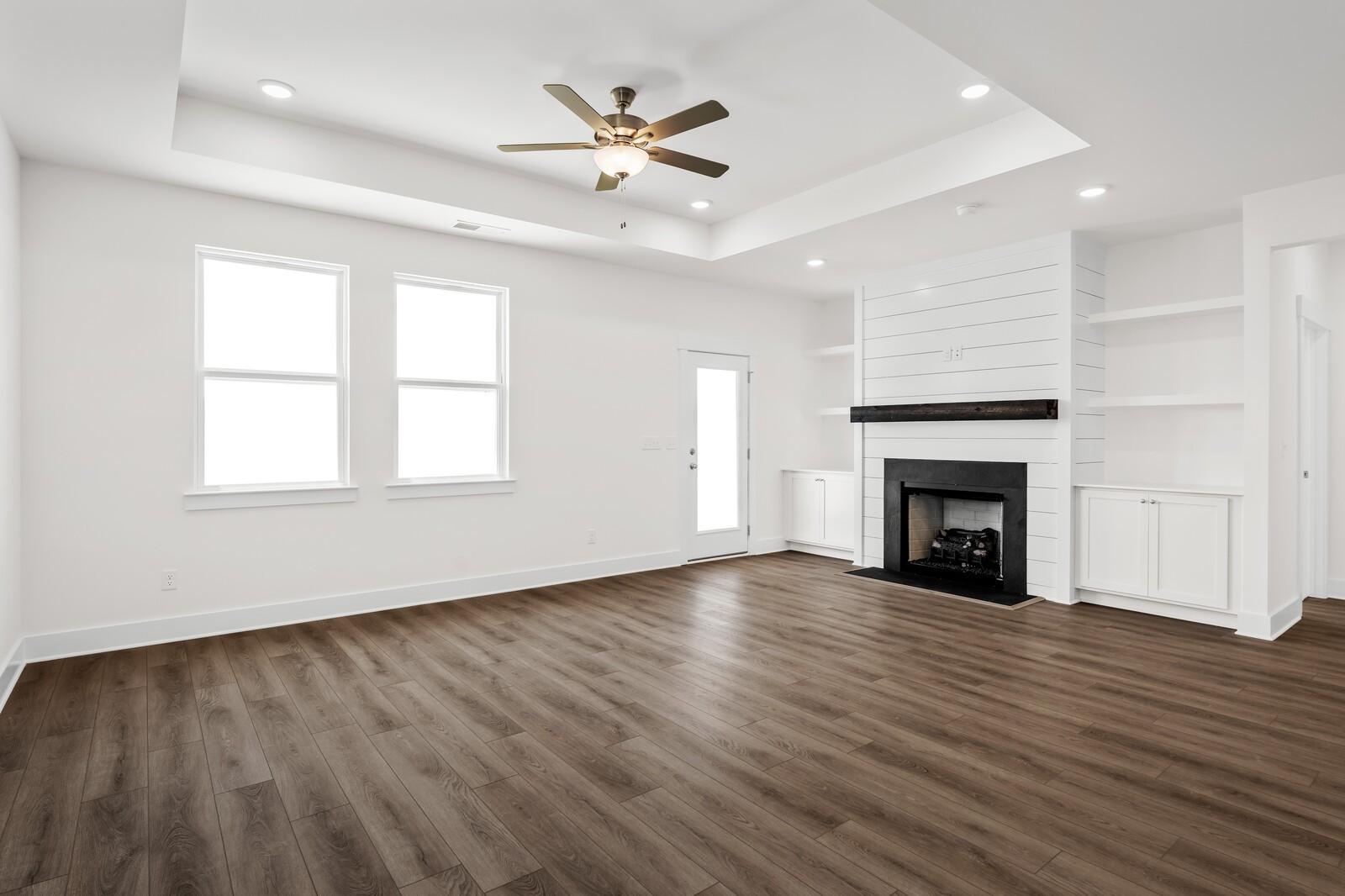 Living room with tray ceiling, fireplace, and built-in shelves in The Cottonwood E floor plan at Woods Crossing, Gallatin.