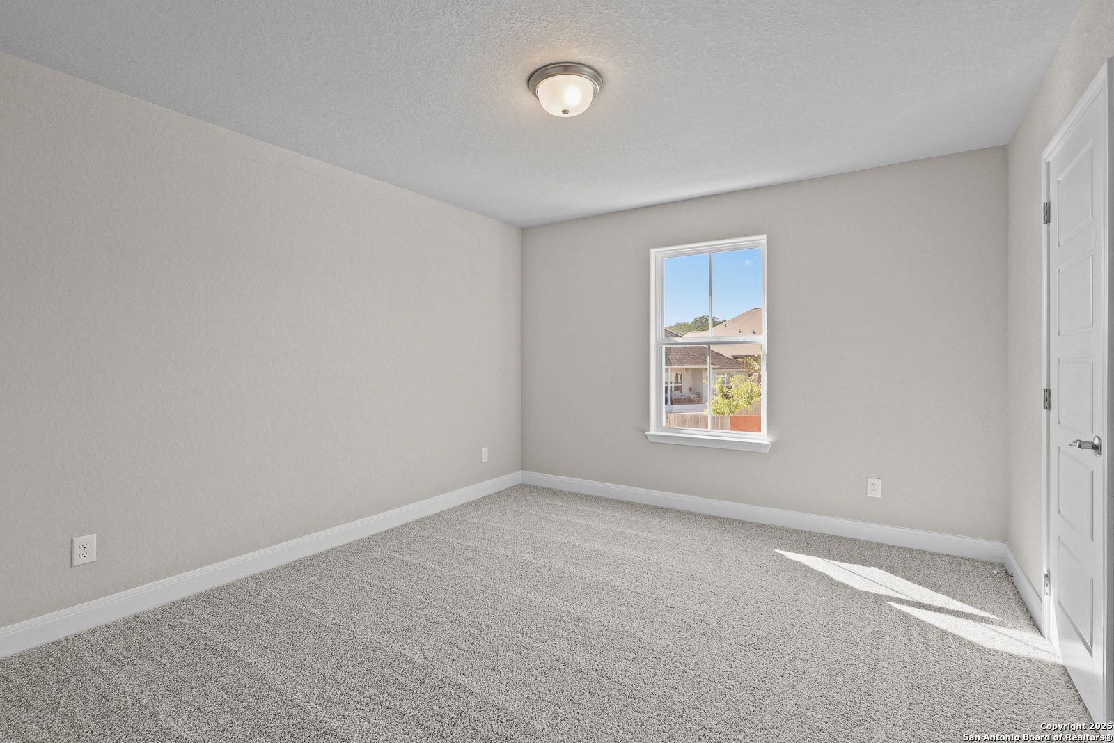 Empty bedroom with light gray walls, carpet floor, ceiling light, and window view of backyard in Davidson Homes The Jennings G, Castroville, Texas