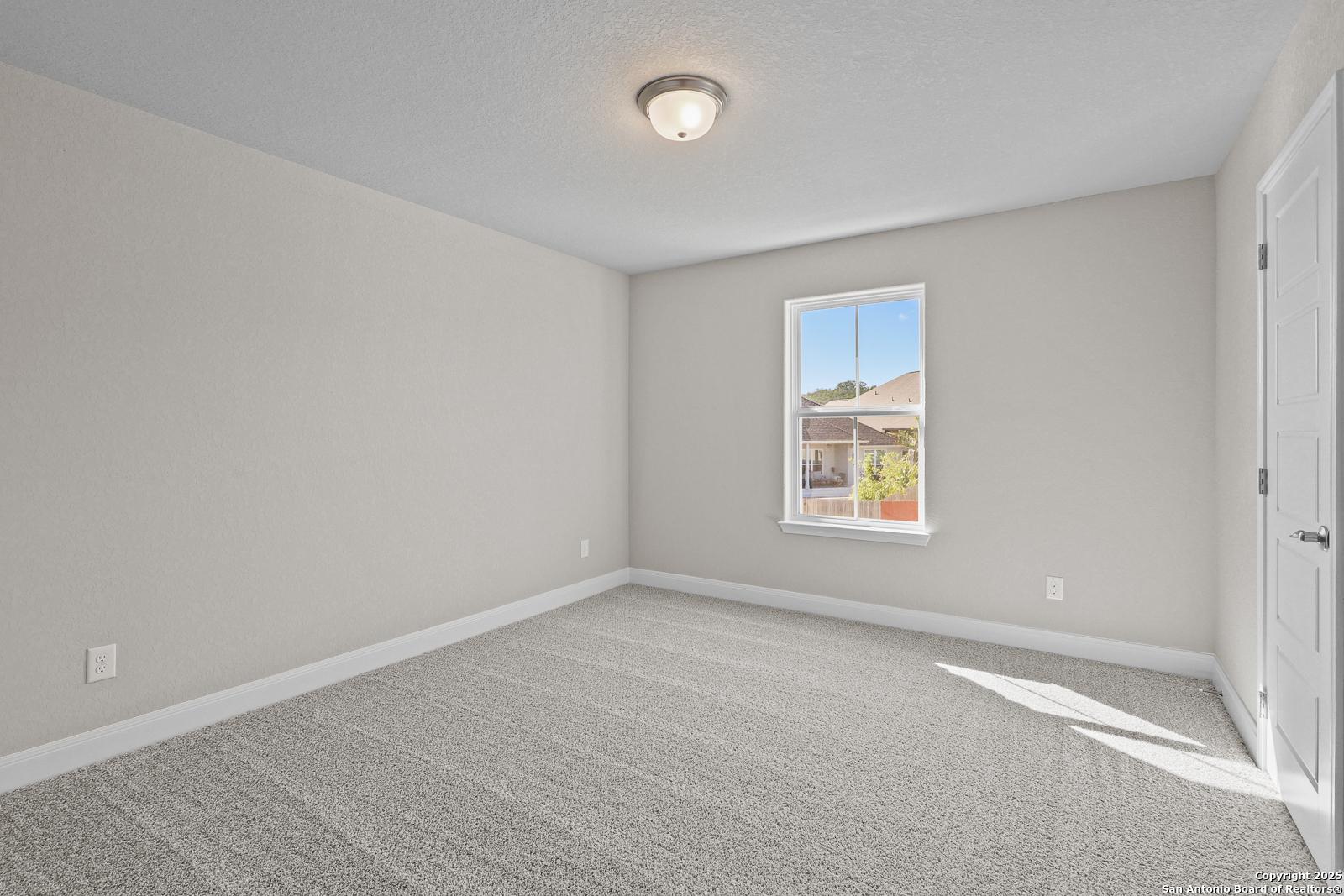 Empty bedroom with light gray walls, carpet floor, ceiling light, and window view of backyard in Davidson Homes The Jennings G, Castroville, Texas
