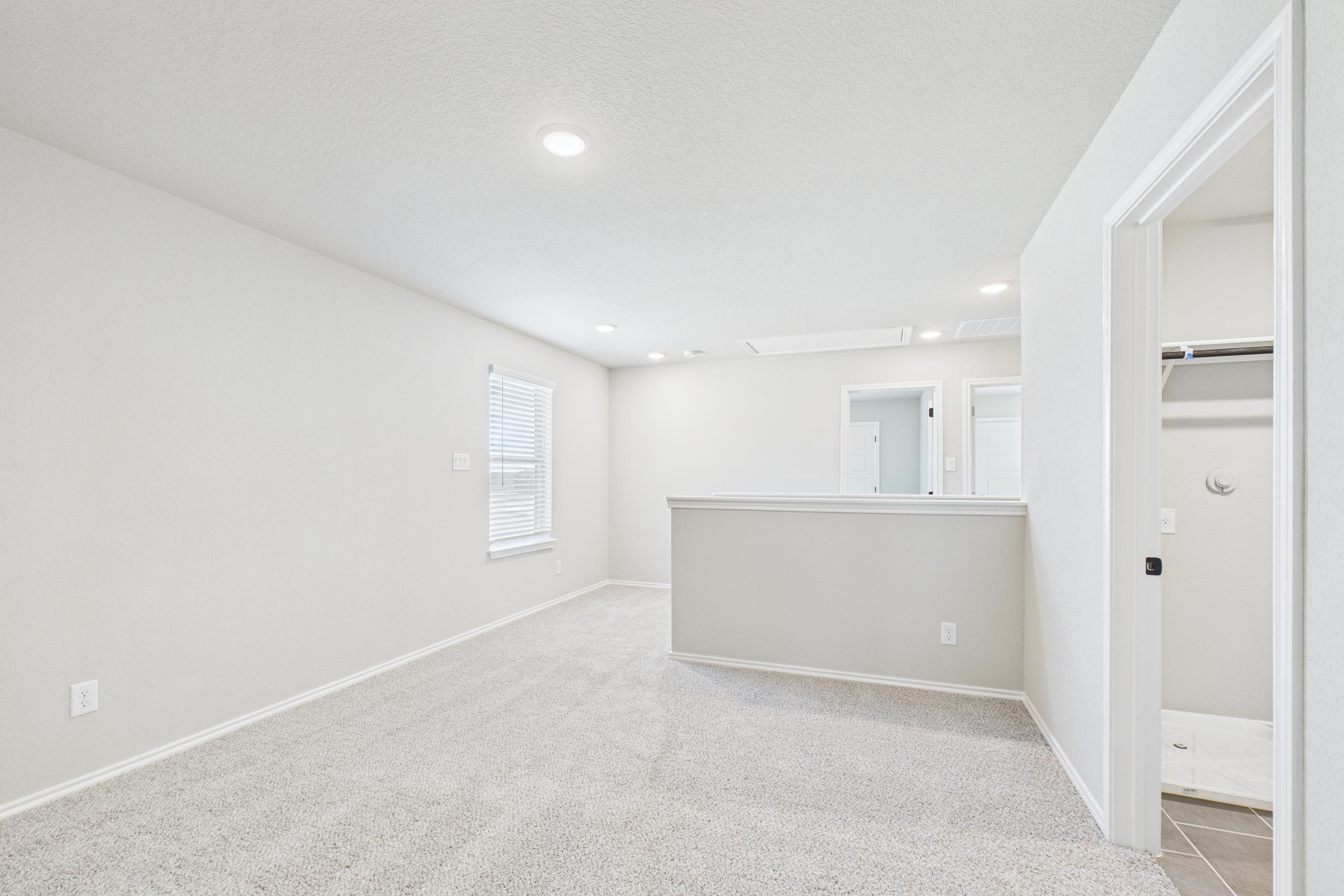 Spacious upstairs loft in The Charlotte home design by Davidson Homes featuring neutral carpet and access to a walk-in closet.