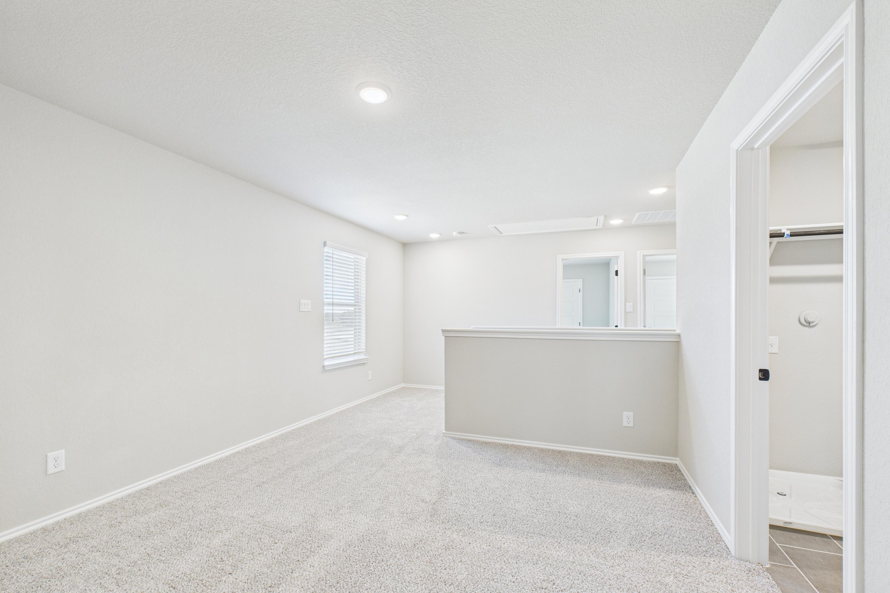 Spacious upstairs loft in The Charlotte home design by Davidson Homes featuring neutral carpet and access to a walk-in closet.