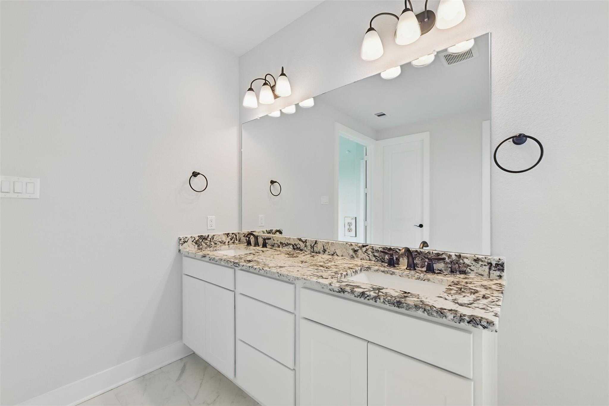 Modern master bathroom double vanity with swirled granite countertops, dual sinks, mirrors, and sconce lights in Davidson Homes The Victoria C, Lago Mar, Texas City