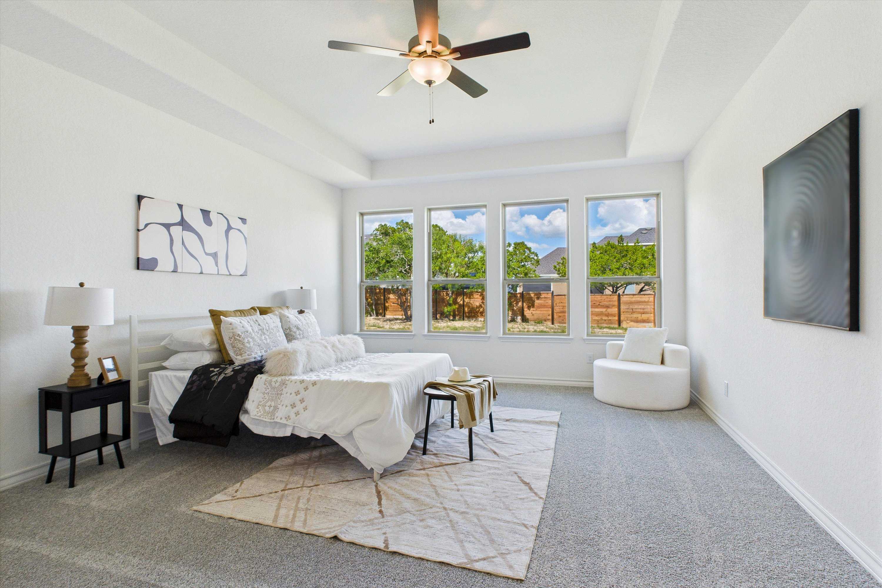 Spacious master bedroom with king bed, large windows overlooking trees, ceiling fan in Davidson Homes The Summerlin C, Castroville Texas