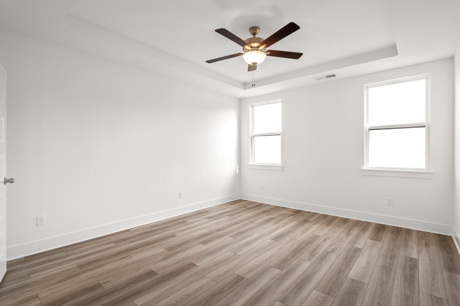 Bright bedroom with luxury vinyl plank floors, white walls, ceiling fan, and double windows in Davidson Homes Ash C, Mt. Juliet