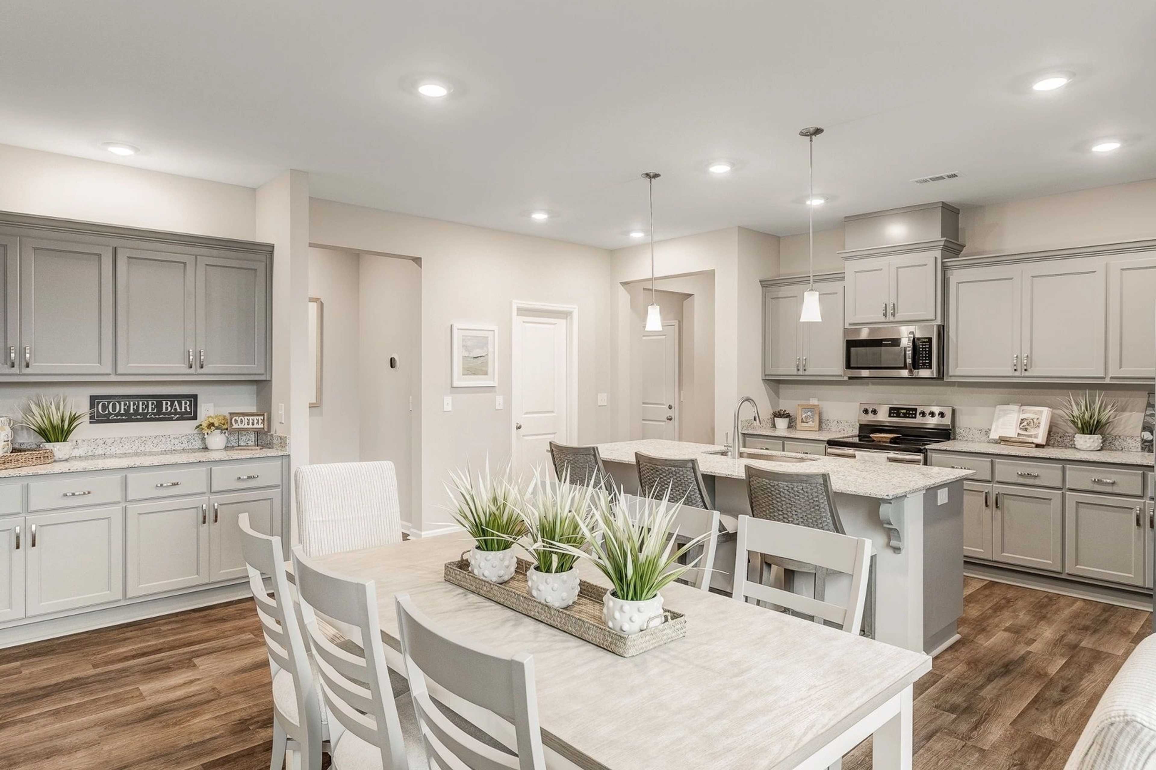 Spacious open-concept kitchen and dining area in Carroll Green, Harvest AL with gray cabinets, island bar, hardwood floors, and coffee station