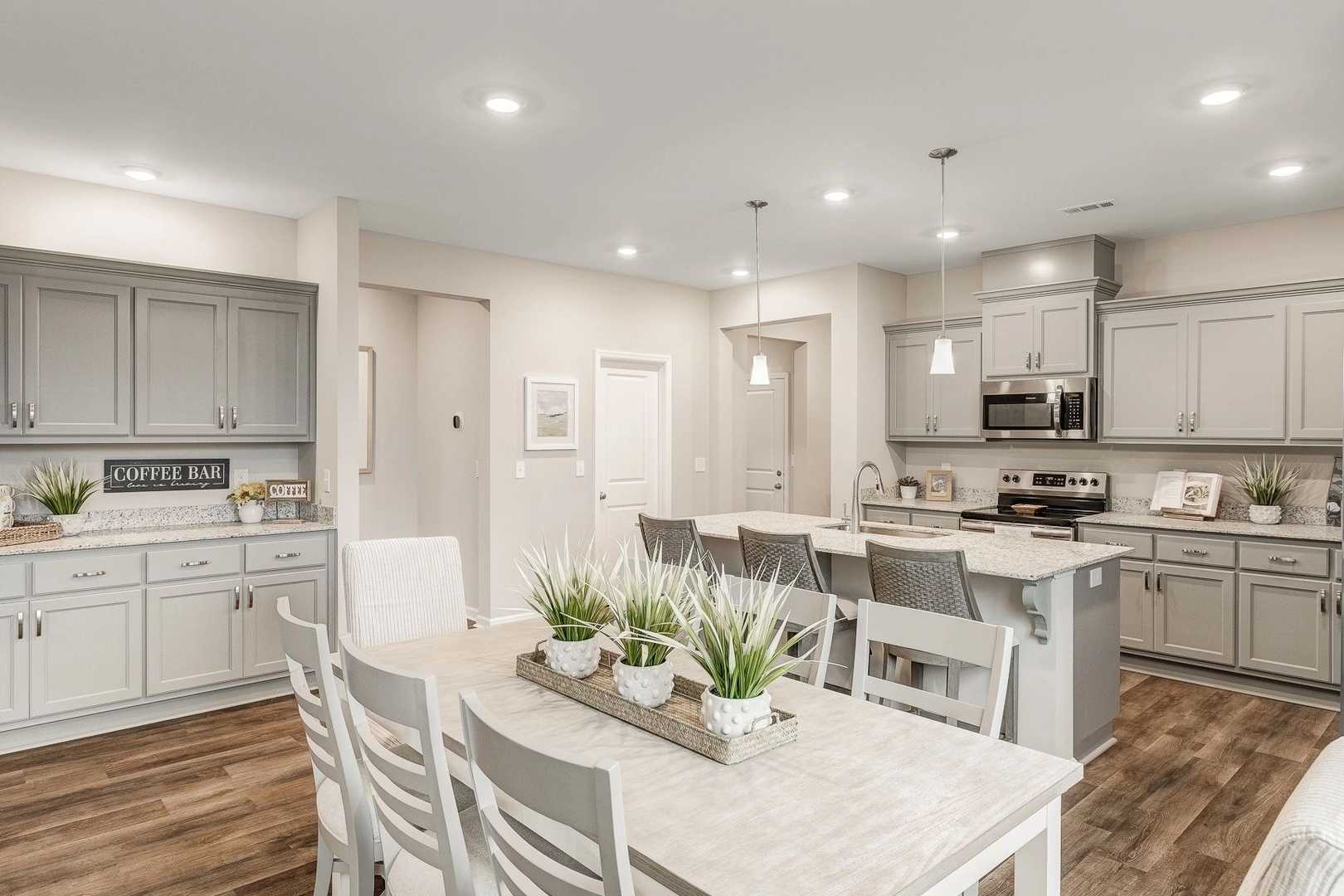 Spacious open-concept kitchen and dining area in Carroll Green, Harvest AL with gray cabinets, island bar, hardwood floors, and coffee station
