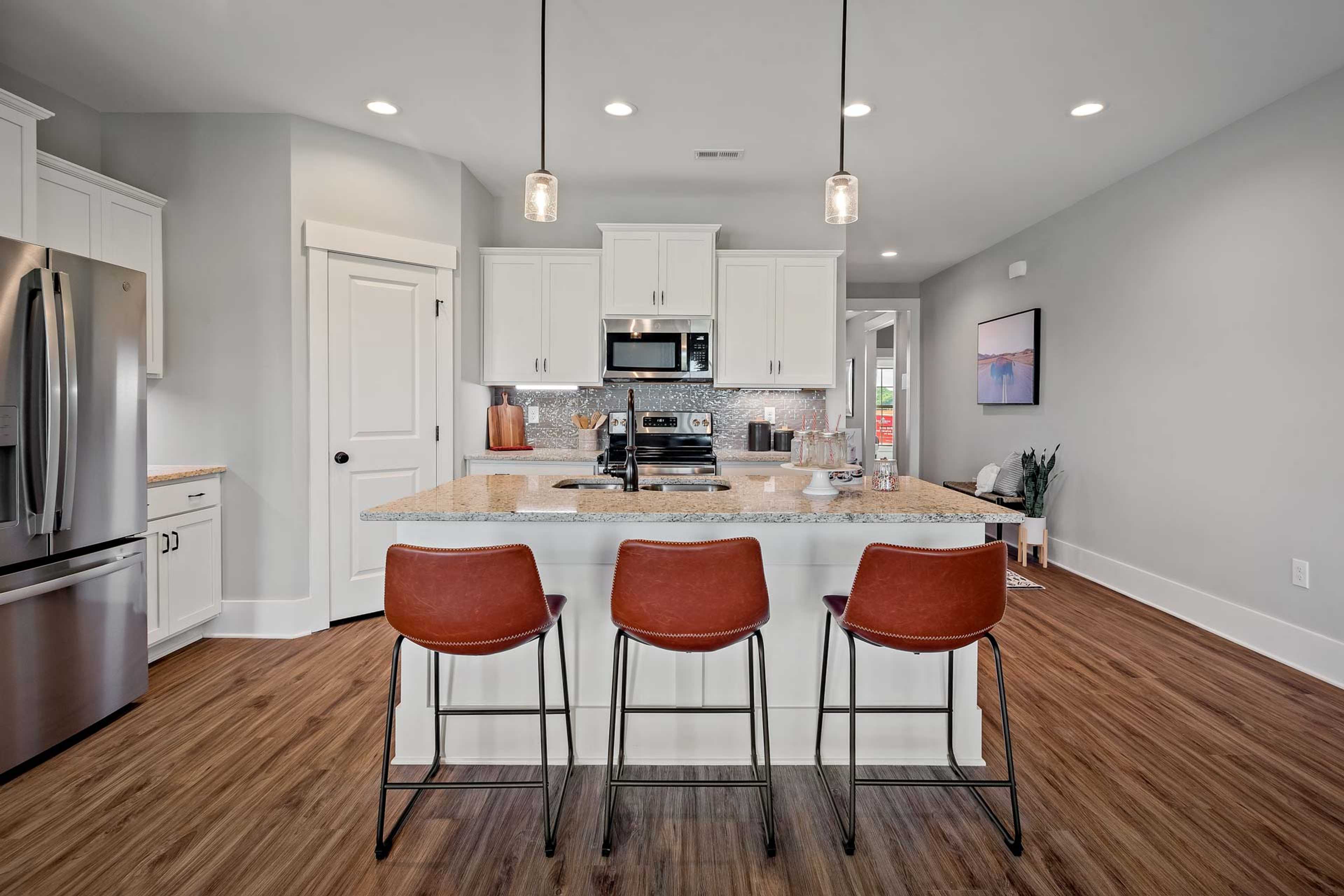 Modern kitchen with white cabinets, stainless steel appliances, island seating, and hardwood floors at Heritage Lakes, New Market AL