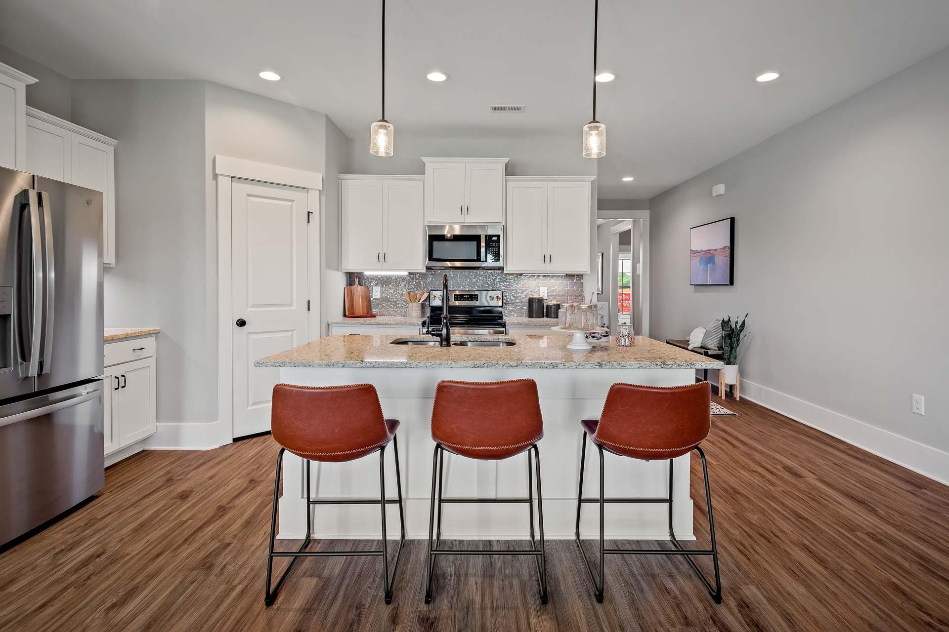 Modern kitchen with white cabinets, stainless steel appliances, island seating, and hardwood floors at Heritage Lakes, New Market AL