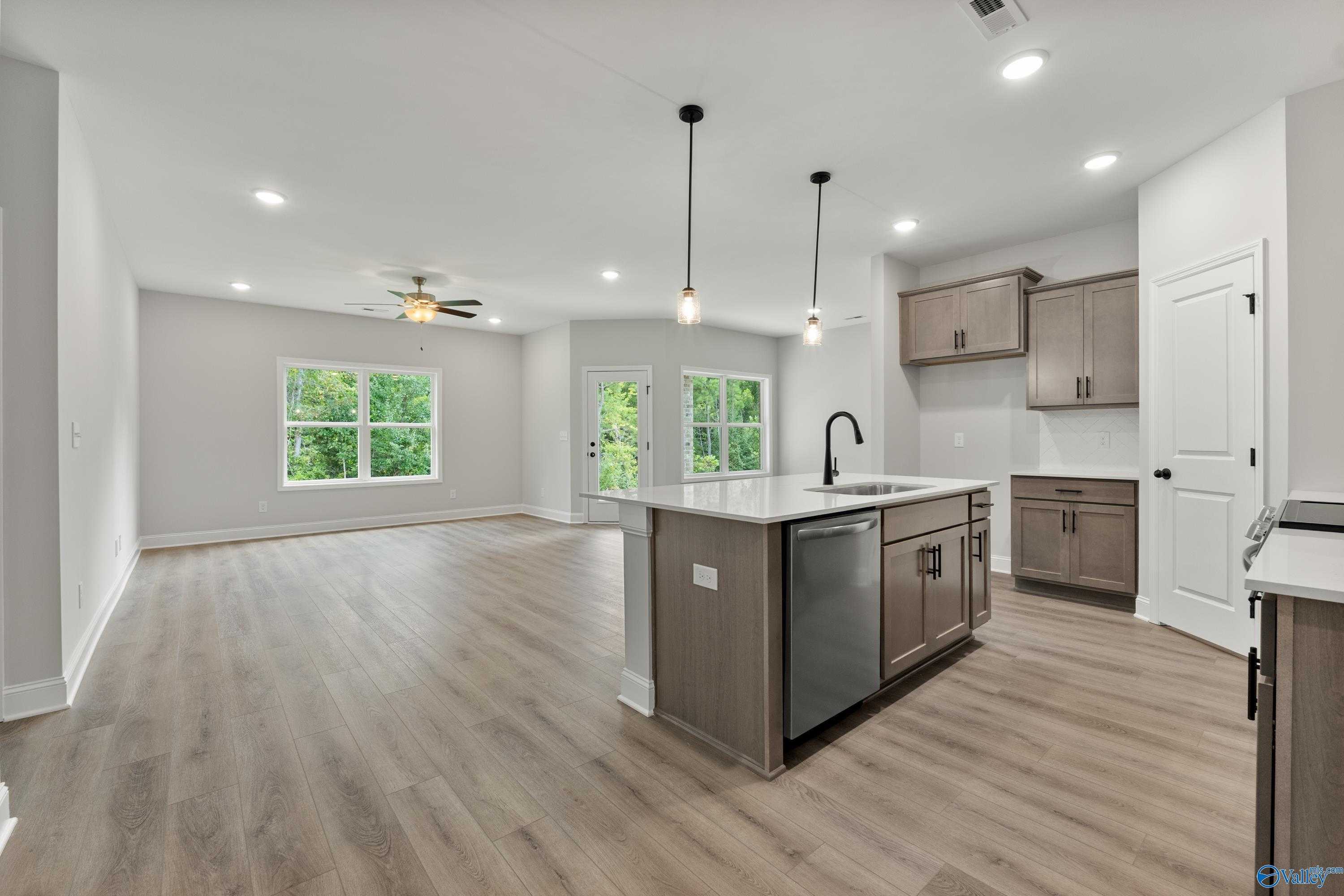 Open-concept kitchen with central island sink, shaker cabinets, stainless dishwasher, and large windows in The Daphne home, Huntsville, AL