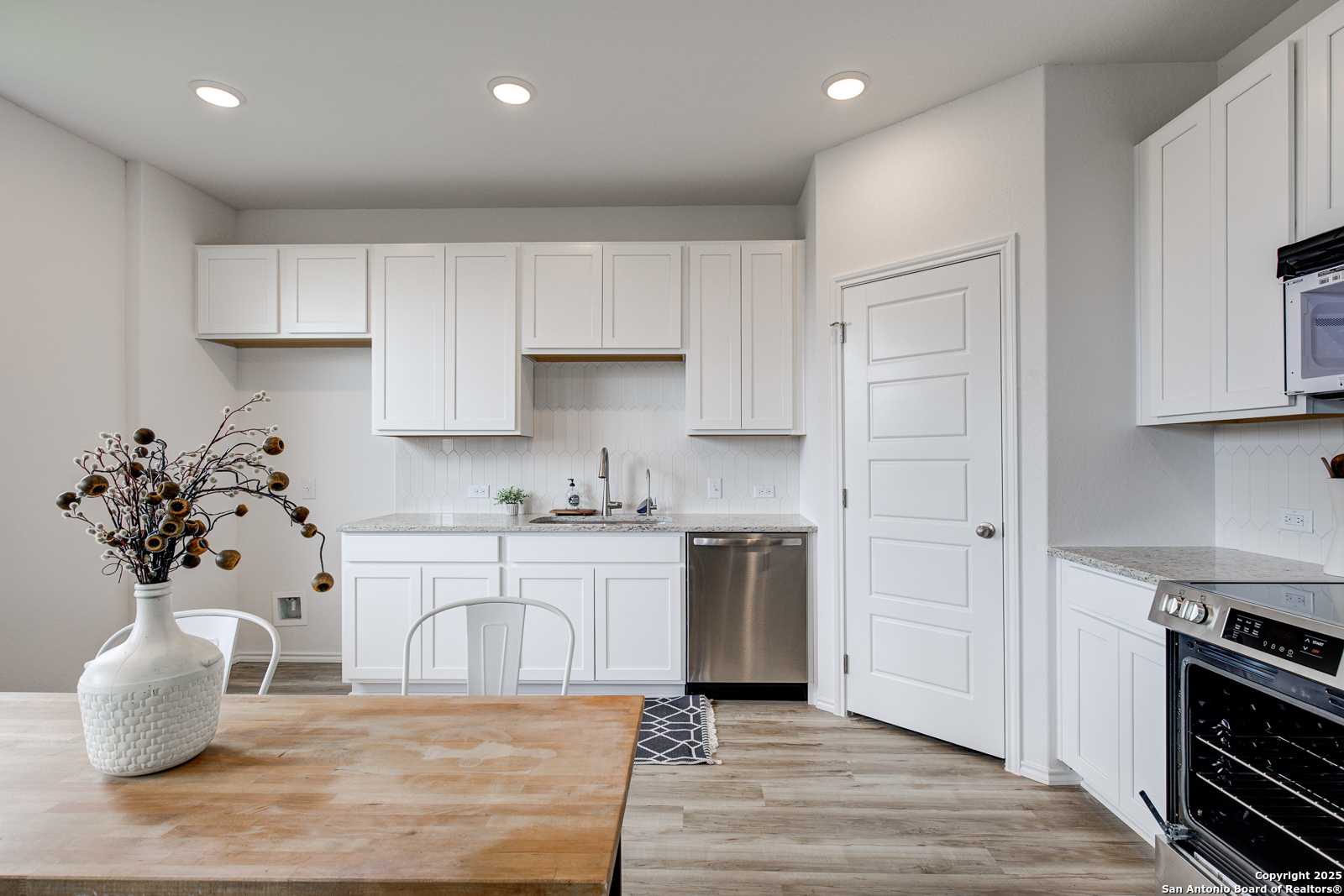 Modern white kitchen with stainless steel appliances, quartz counters, and dining nook in Davidson Homes The Trinity A, San Antonio