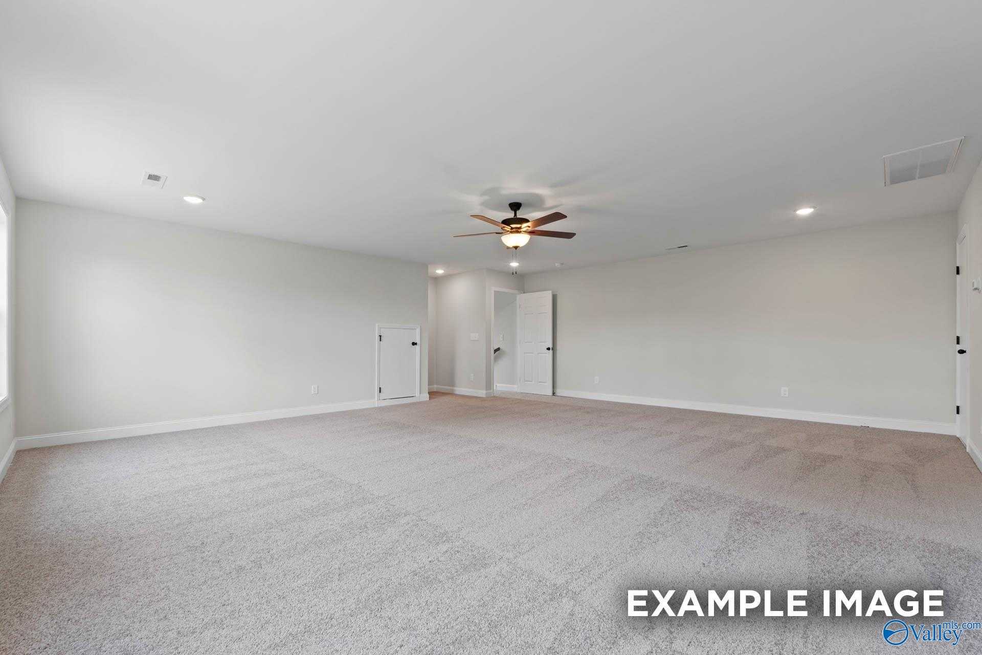 Spacious empty living room with beige carpet, ceiling fan, and white walls in Davidson Homes The Kirkland, Decatur AL