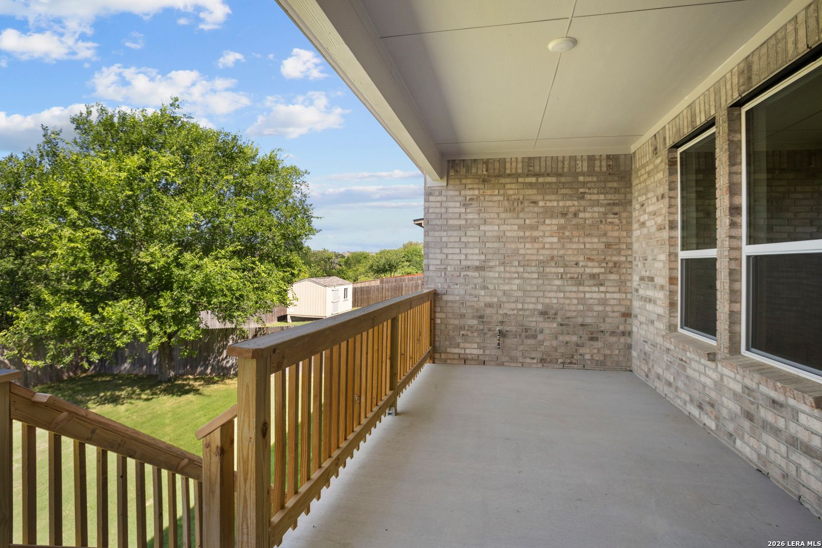 Covered brick balcony with wooden railing overlooking the private backyard of a Davidson Homes Jennings G plan in Ladera.