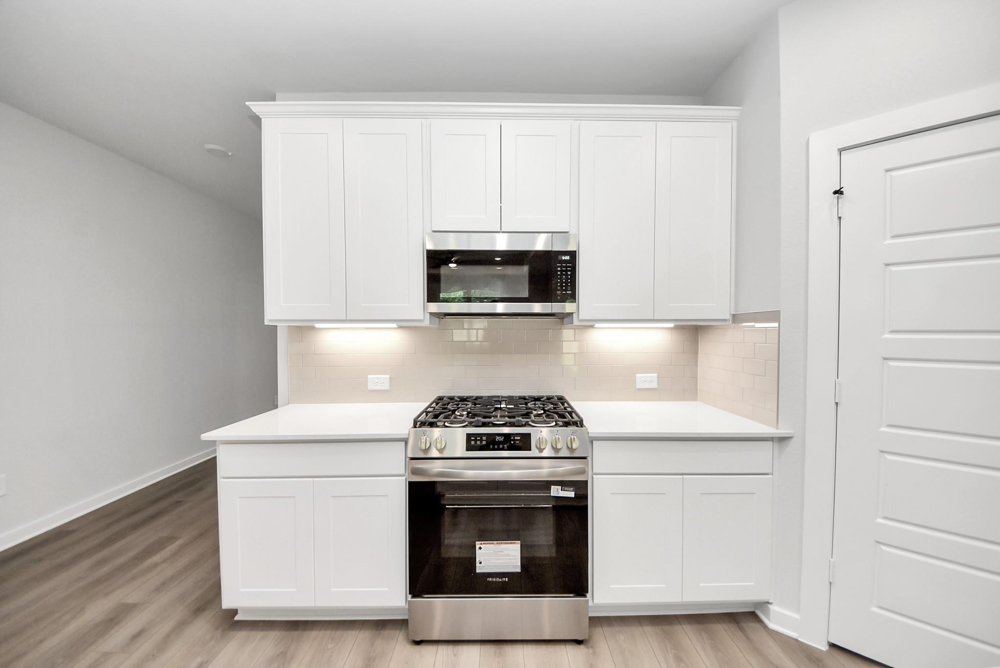 Modern kitchen with white cabinets, stainless steel appliances, and tile backsplash in The Daphne F home at Sundance Cove.