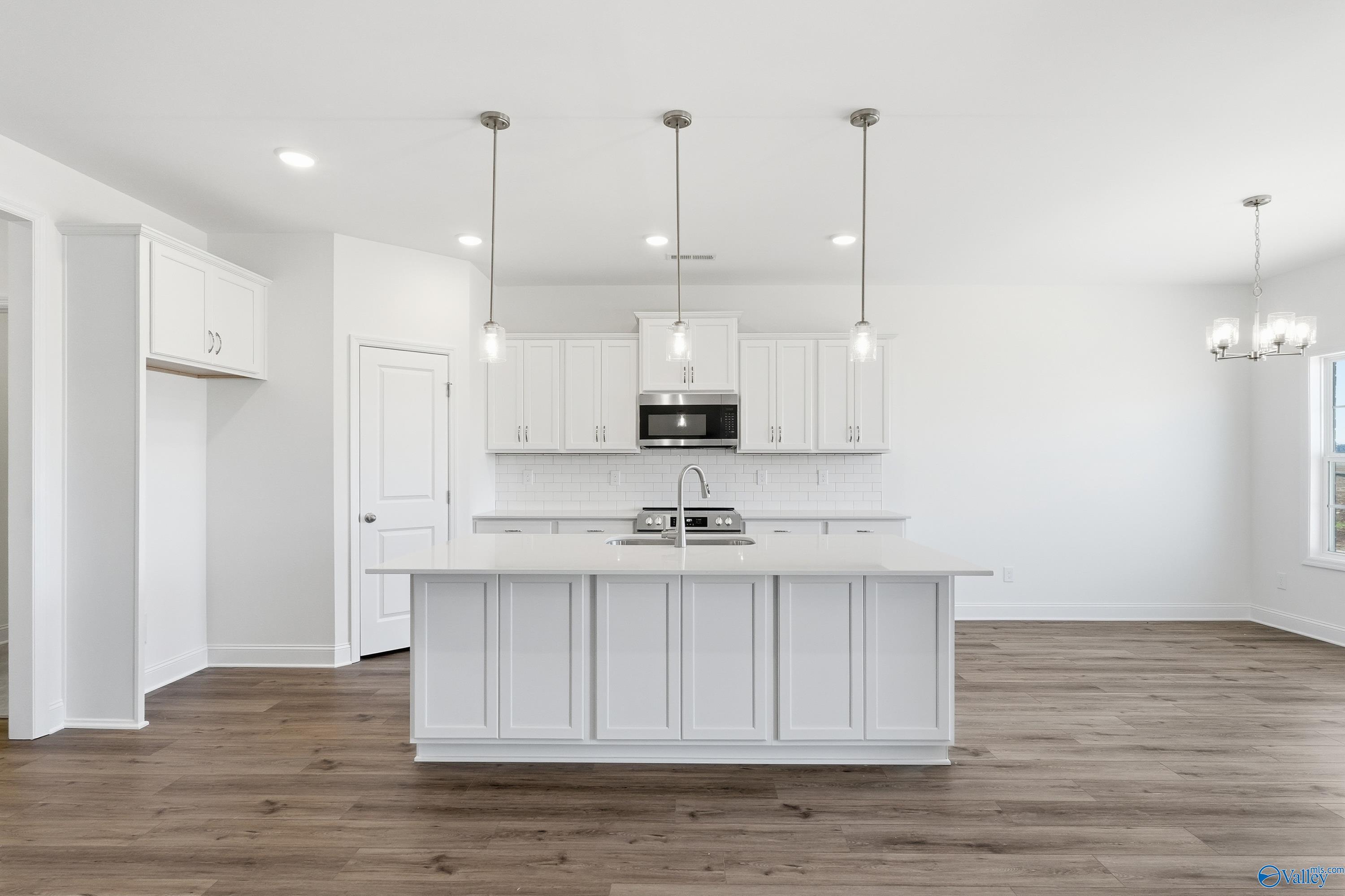 Modern white shaker kitchen with oversized island sink, stainless appliances, pendant lights, hardwood floors in Davidson Homes The Montgomery, Meridianville AL