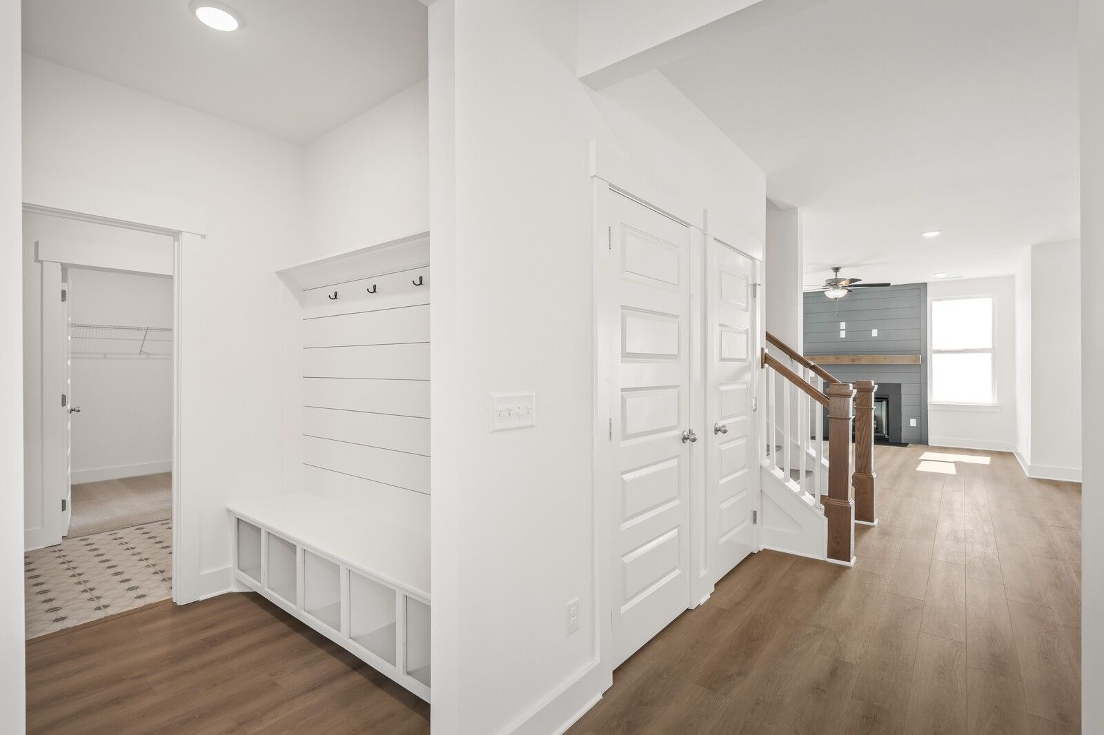 Bright mudroom with shiplap walls, built-in bench, coat hooks, and adjacent wooden staircase to fireplace in Davidson Homes The Ash A, Gallatin, TN