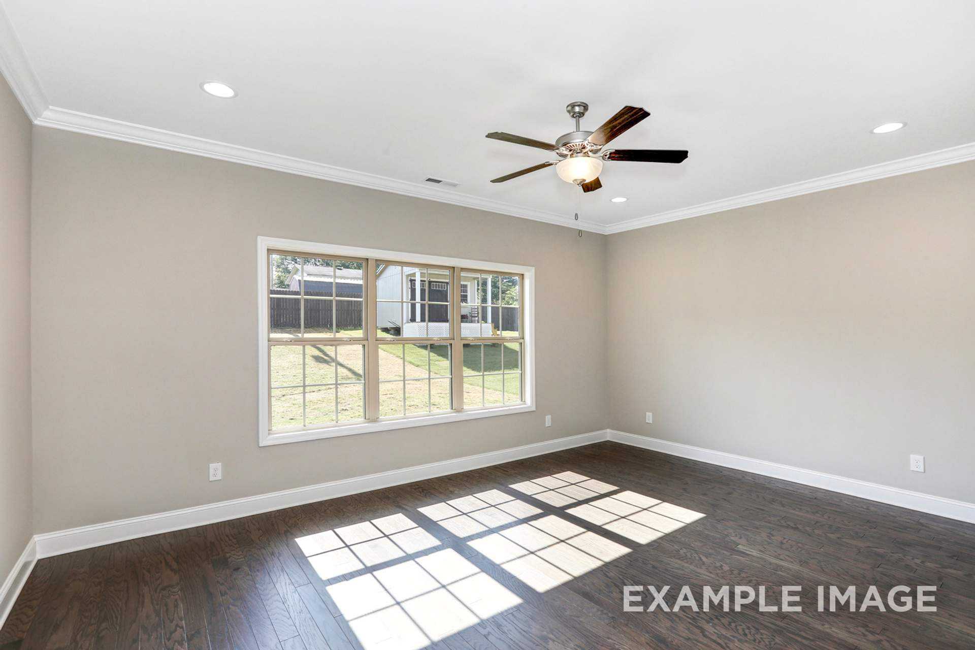 Bright master bedroom in The Montgomery C with light gray walls, hardwood floors, large windows, and dual ceiling fans