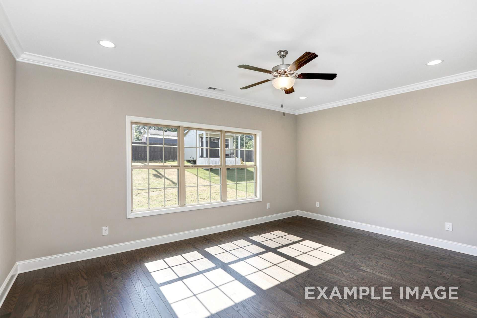 Bright master bedroom in The Montgomery B with hardwood floors, large sunny windows, and ceiling fan