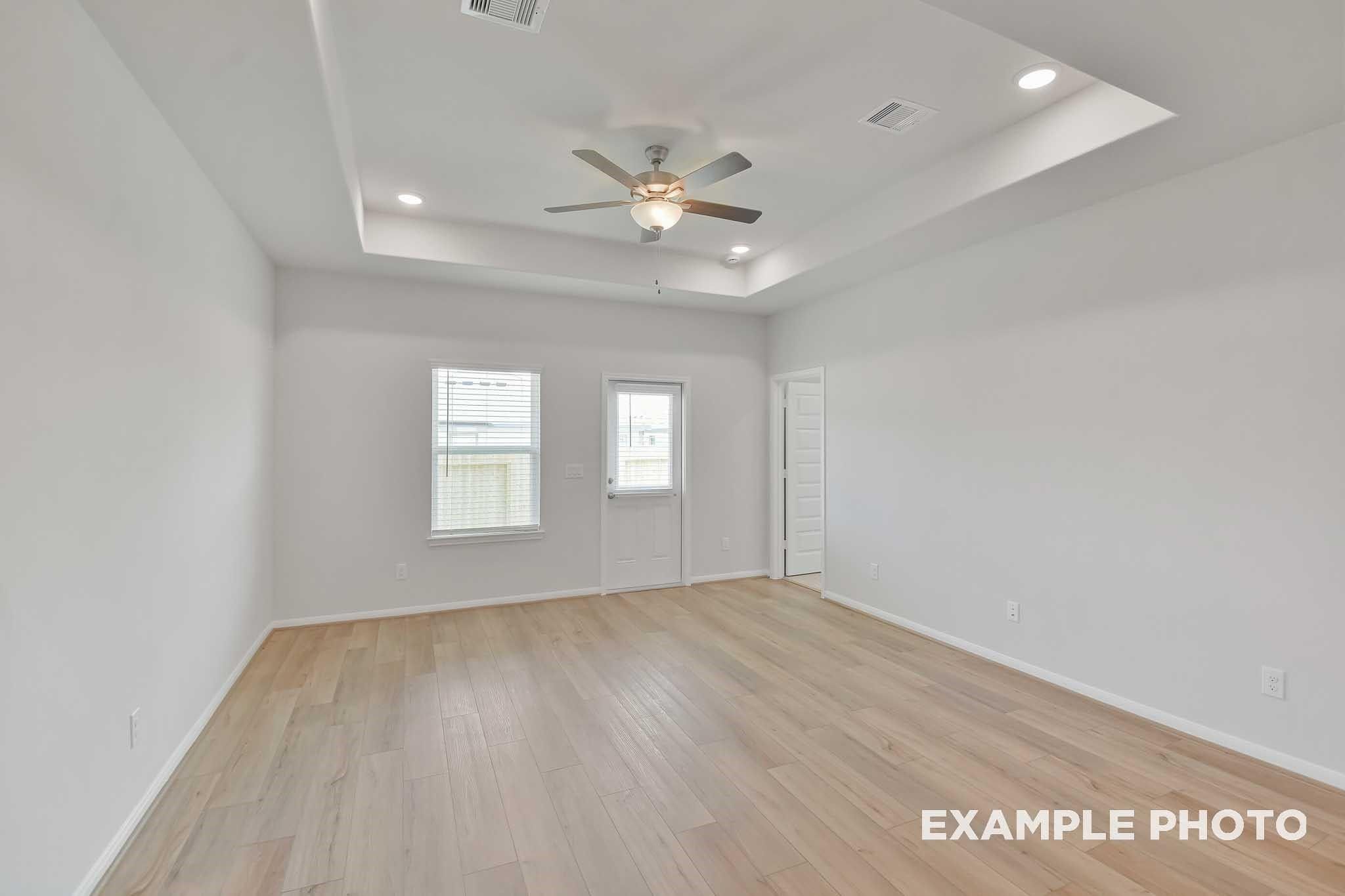 Bright bedroom with light hardwood floors, ceiling fan, recessed lights, and windows in Davidson Homes The Frio F, Conroe, Texas