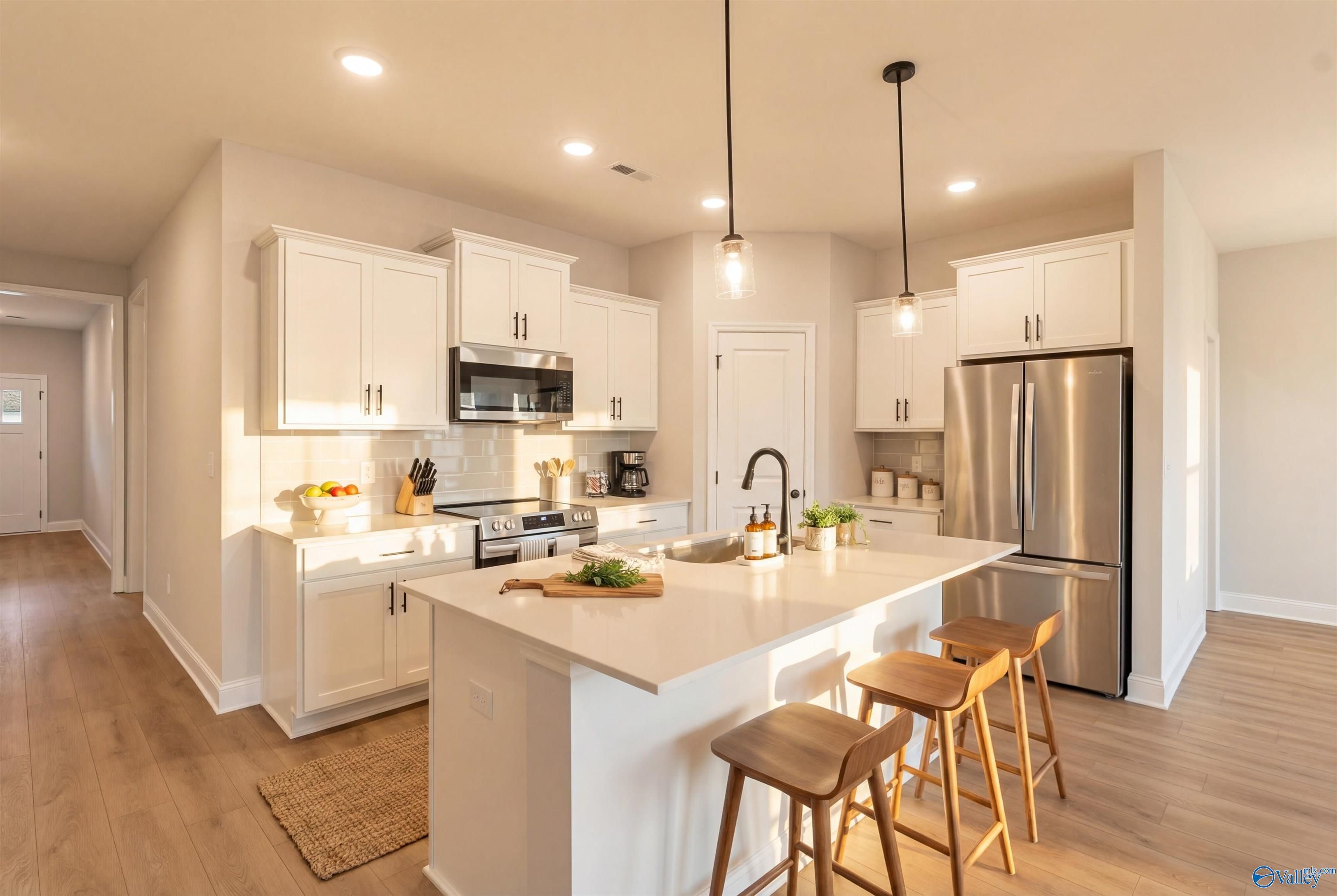 Modern white kitchen with stainless steel appliances, large island, and open layout in The Daphne D by Davidson Homes, Arab, Alabama