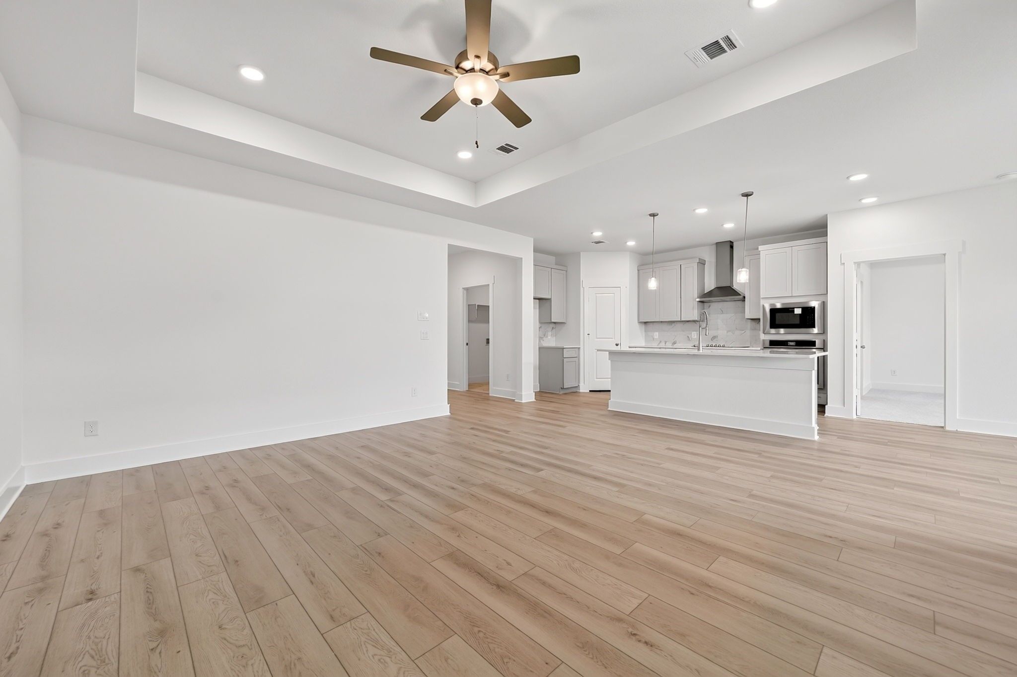 Open-concept living room and kitchen with wood-look flooring and ceiling fan in Davidson Homes The Holly F, Josephine, Texas